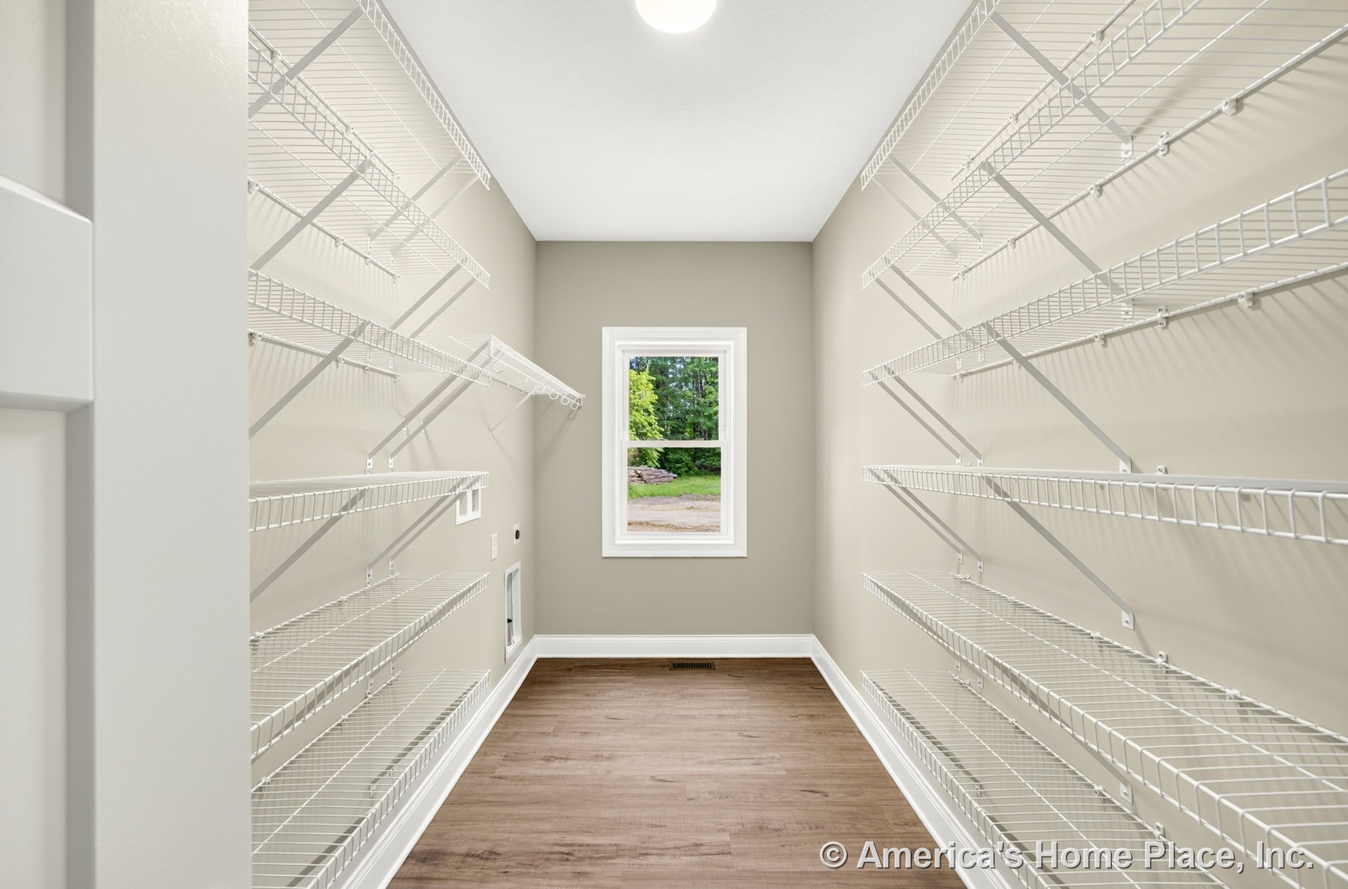 Pantry utility room with multiple white wire shelving units, single window framed in white trim, neutral painted walls, wood-look flooring, recessed ceiling light, and baseboard