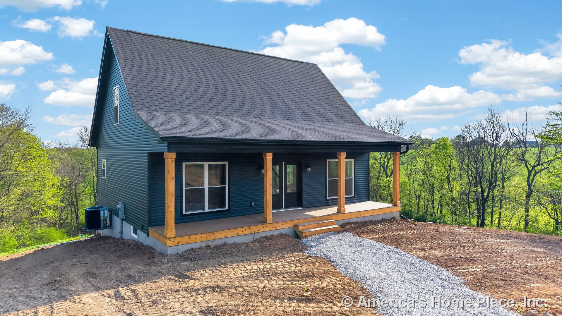 Covered front porch with wood support columns, dark vinyl siding, double front windows, gravel walkway, gable roof, and white trim in a rural setting.