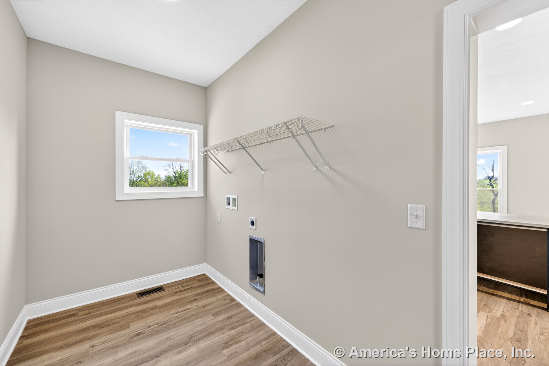 Utility room with wire shelving above laundry appliance hookups, single window framed in white trim, light wood-look flooring, neutral painted walls, and baseboard trim.