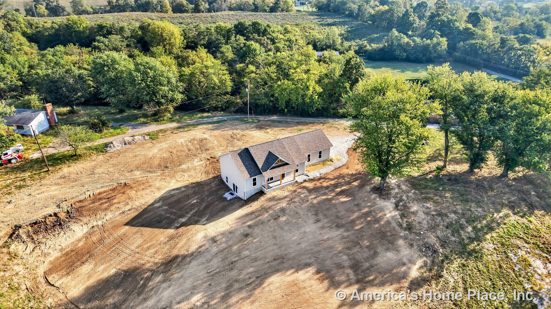 Single-story home with white exterior siding, gable roof, covered front porch, multiple windows, entry door, and unfinished yard on a cleared rural lot.