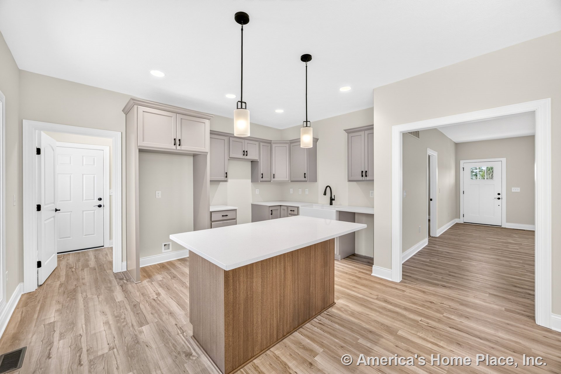 Light gray shaker cabinets with black hardware, central island topped with white quartz countertop, wood-look vinyl plank flooring, black faucet, pendant and recessed ceiling