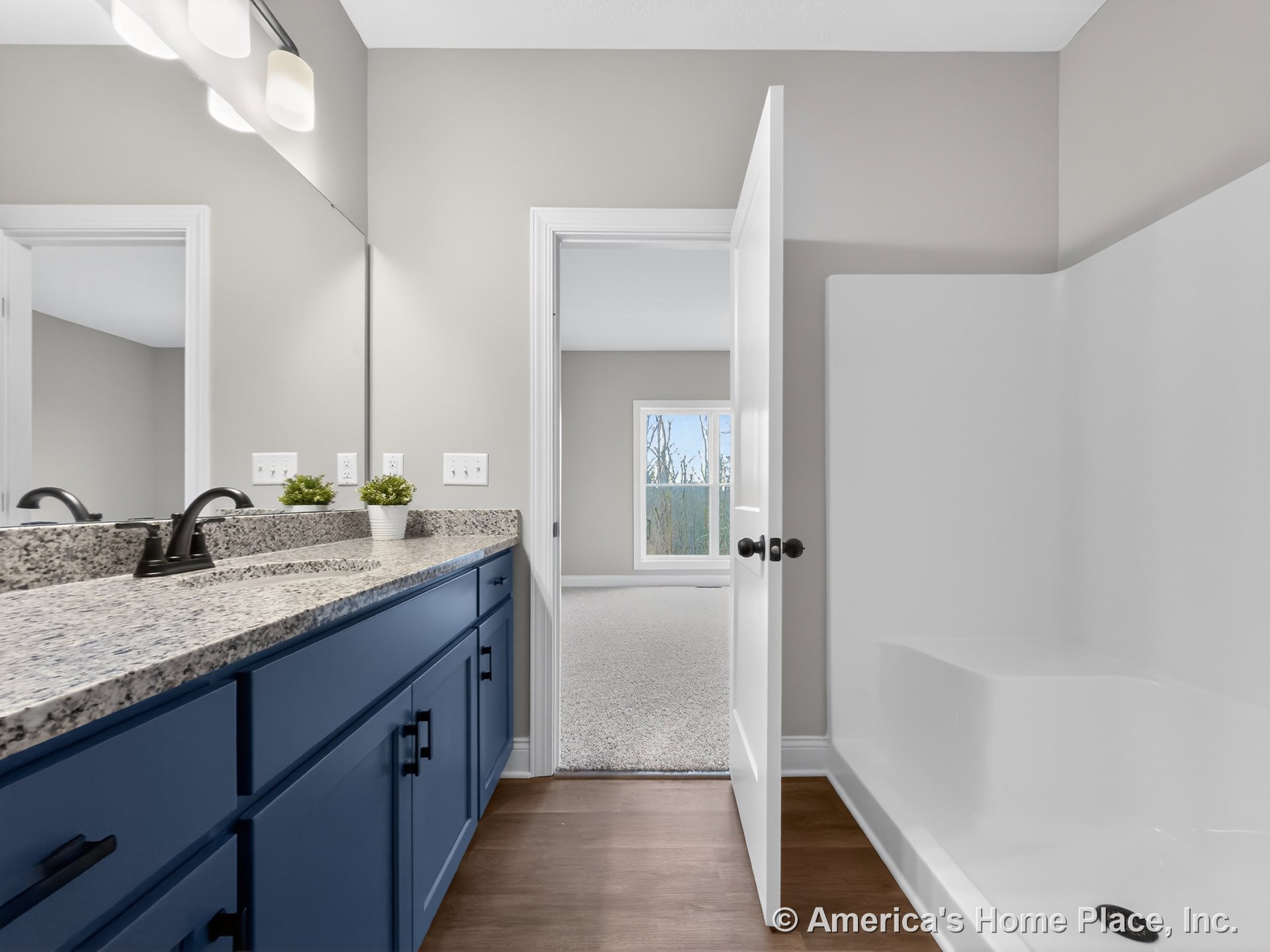 Blue vanity with granite countertop, large wall-mounted mirror, built-in shower enclosure with glass door, matte black faucet, recessed lighting, neutral walls, wood flooring, and