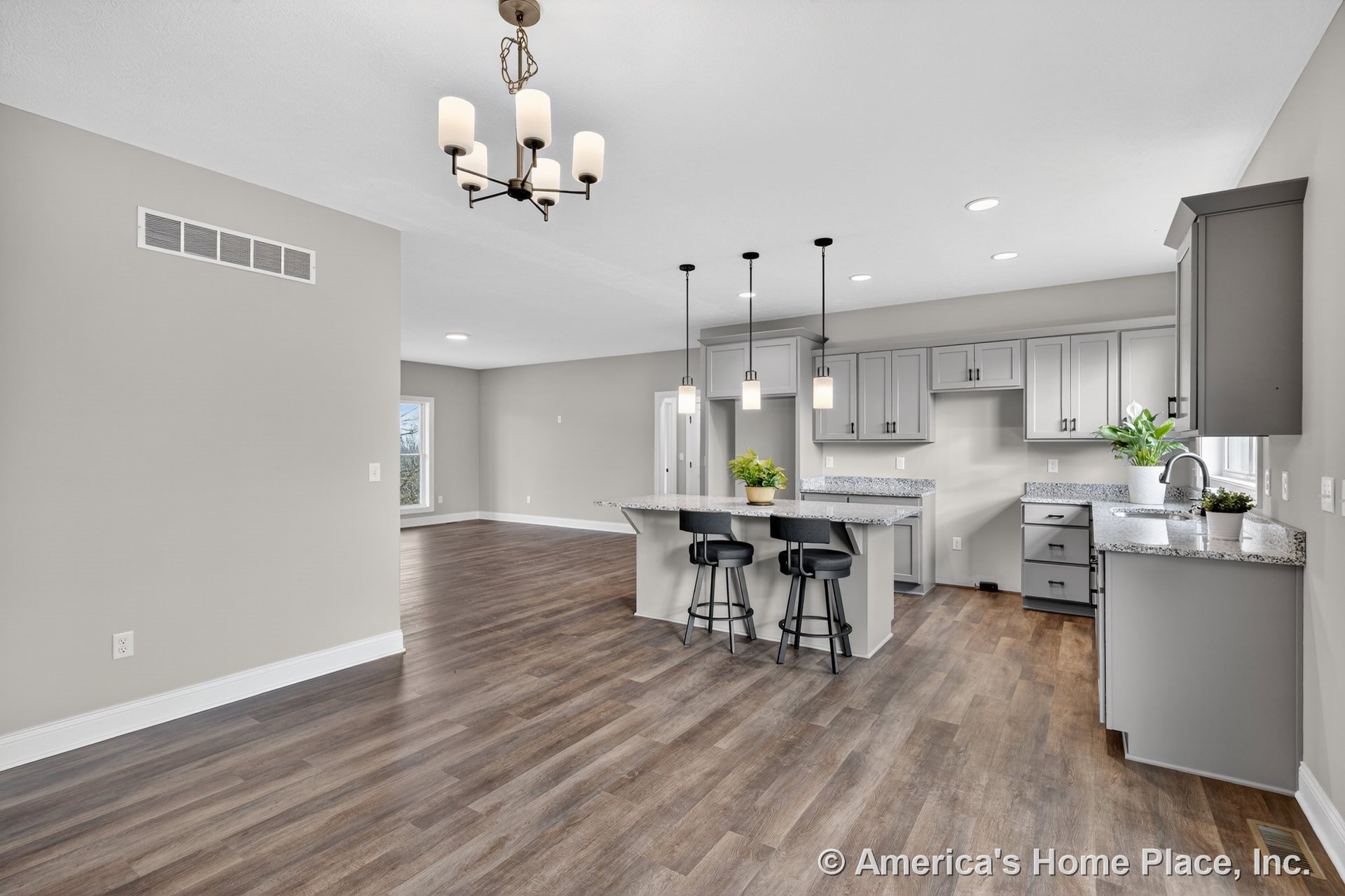 Open kitchen with gray shaker cabinets, granite countertops, large central island with pendant lighting, wood-look flooring, recessed ceiling lights, built-in cabinetry, window