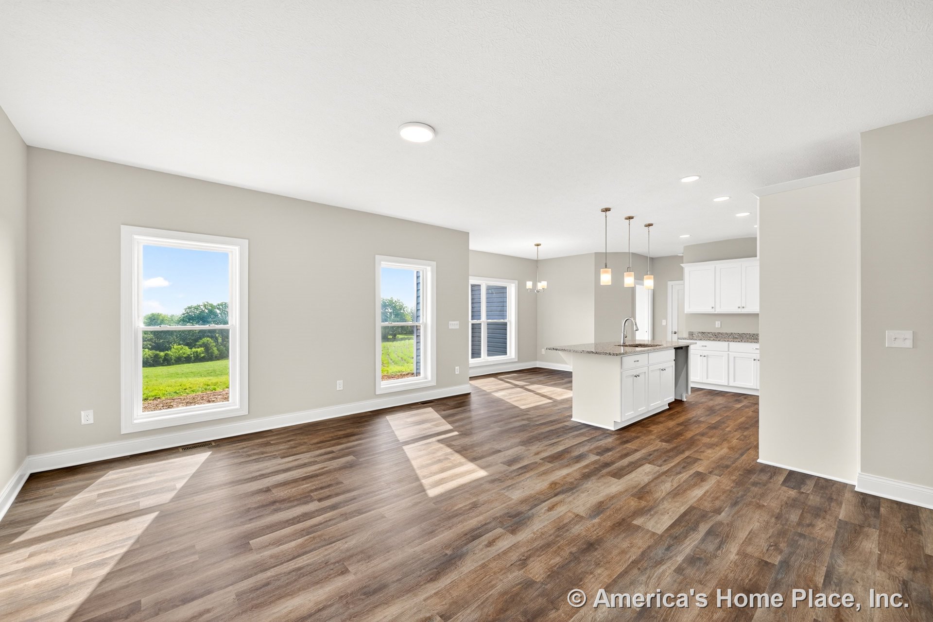 Open-concept kitchen and living area with white shaker cabinets, granite kitchen island countertop, wood-look vinyl plank flooring, large windows with white trim, pendant lights
