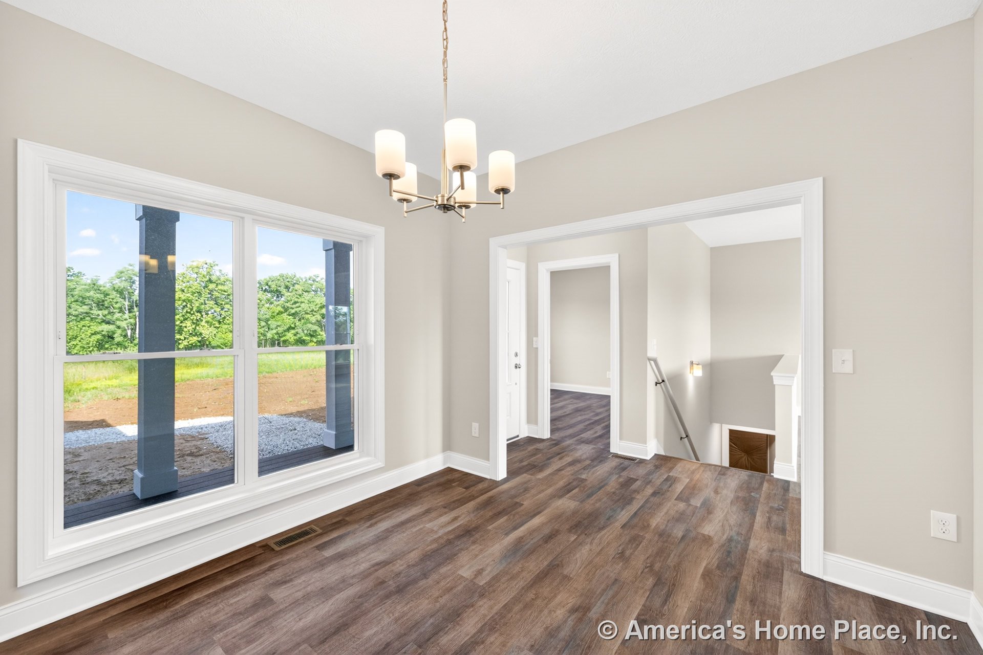 Dining area with large double windows, modern chandelier, wood-look vinyl flooring, white baseboards and trim, open stairway, and neutral wall color.