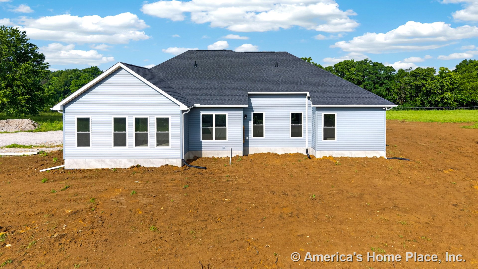 Light blue vinyl siding exterior with dark shingle roof, multiple large rear windows, white trim, concrete foundation, and unfinished backyard.