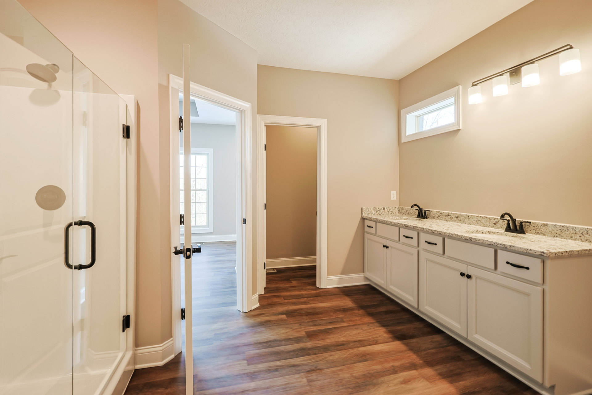White bathroom cabinets with marble countertops, chrome faucet, rectangular window, glass shower door, and tiled floor.