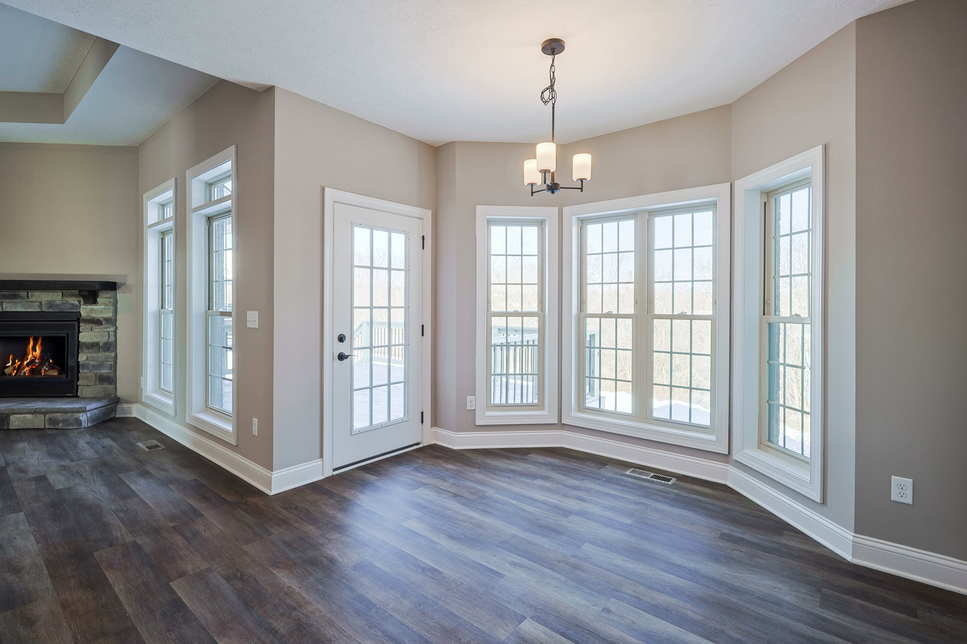 Living room with wood flooring, white-framed windows, glass-paneled door, and fireplace with burning fire