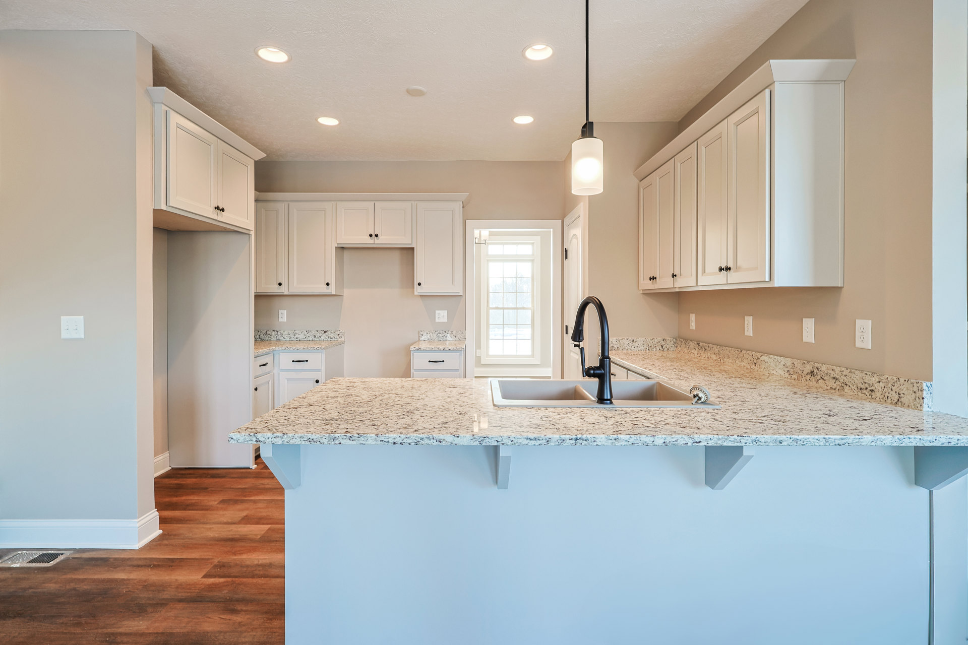 Granite countertop kitchen with black faucet sink, rectangular pendant light, white cabinetry, and window overlooking snowy landscape