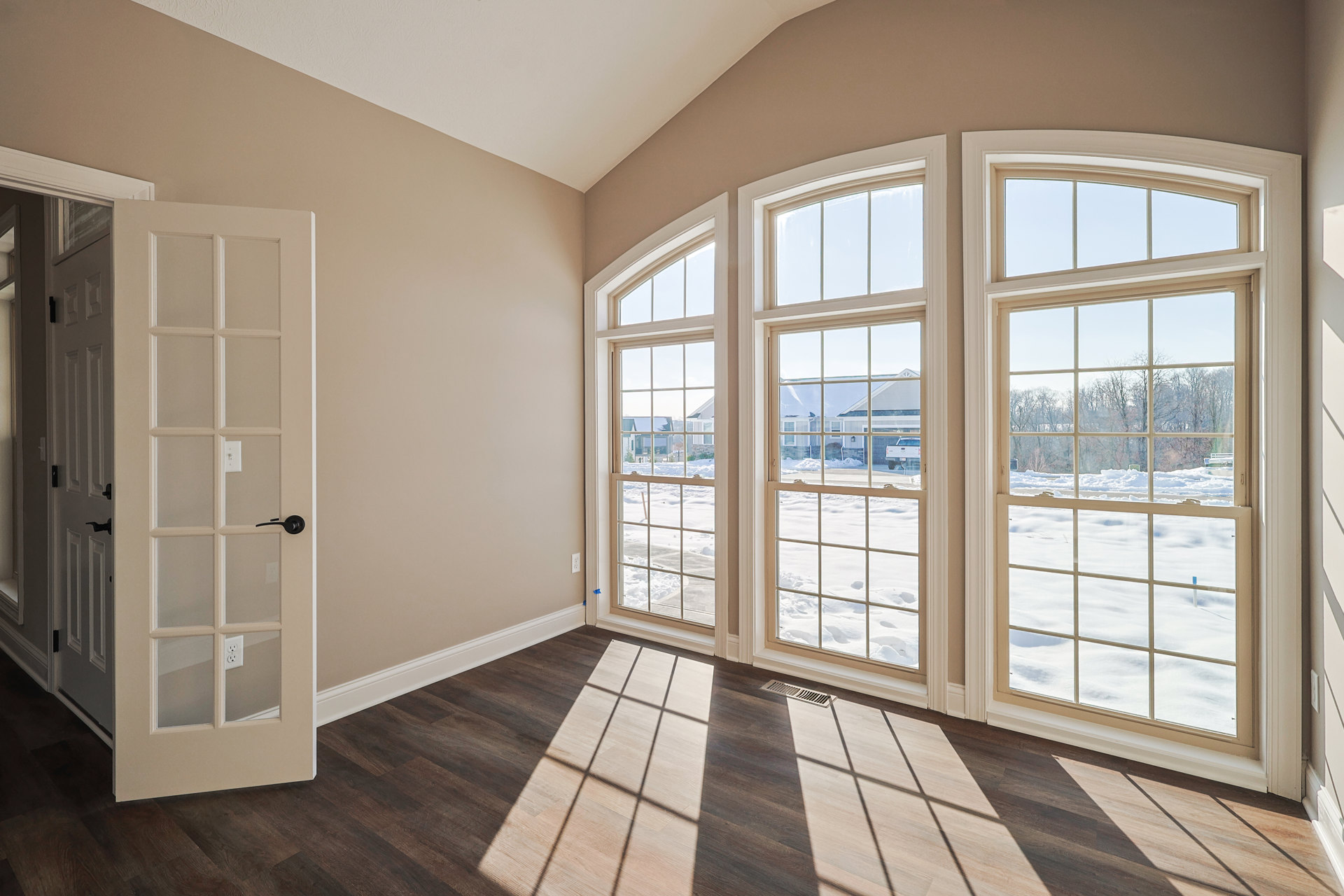 Wood floor room featuring a glass-paneled door and large windows overlooking a snowy field and neighboring house