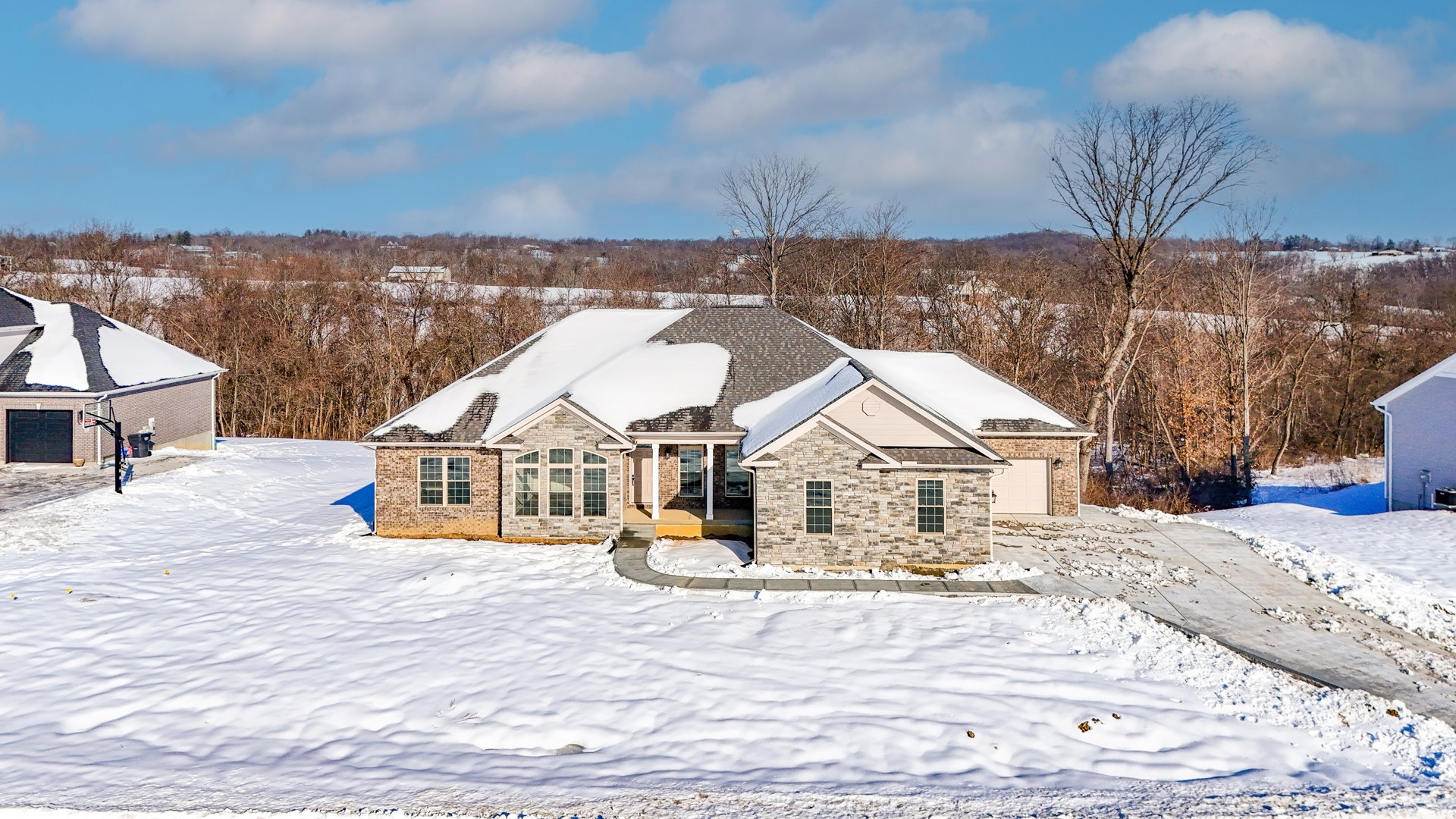 Two-story home with snow-covered roof and driveway, leafless tree in front yard, cloudy winter sky, black rectangular mailbox with white border near entrance