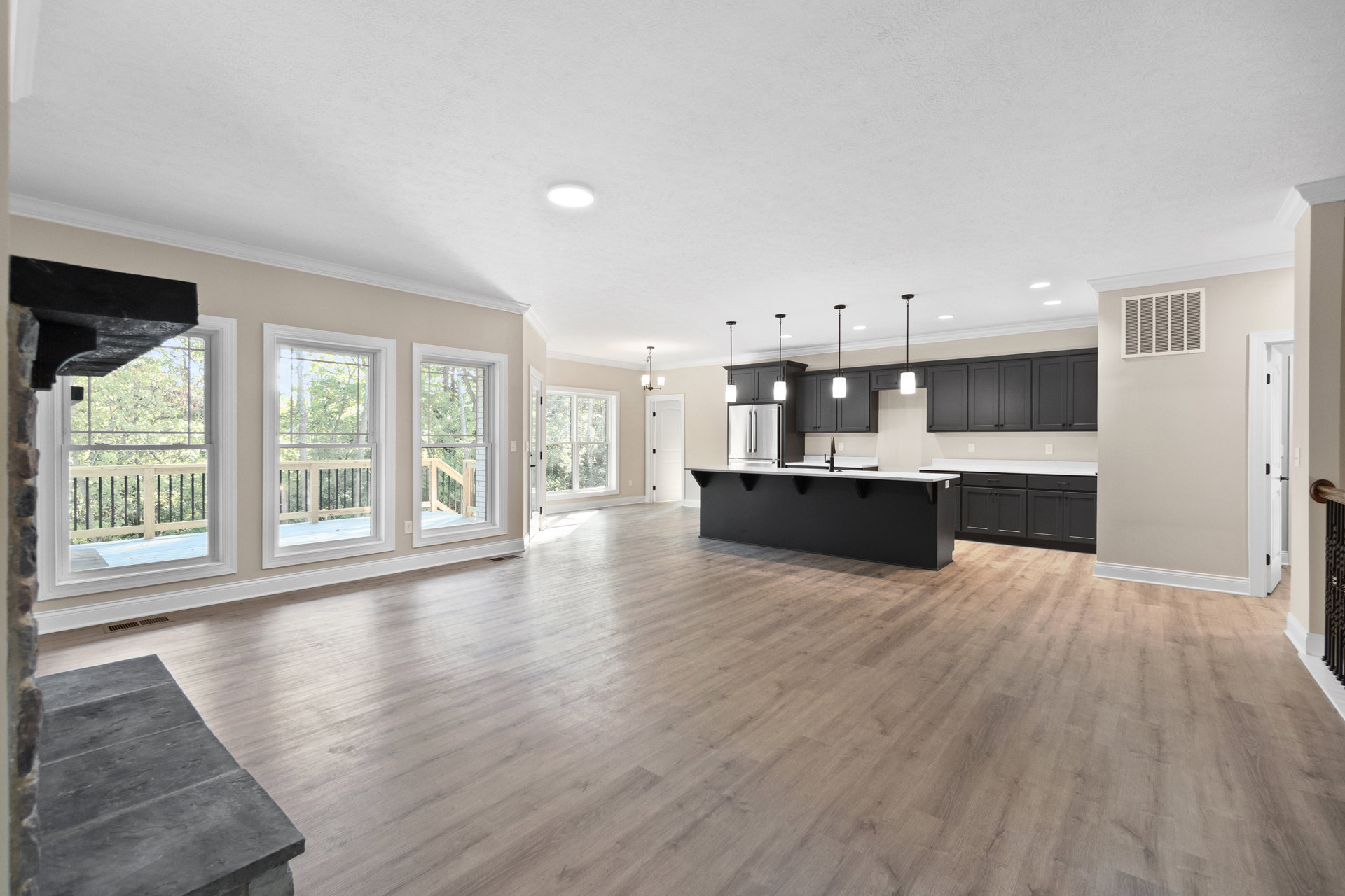 Spacious open floor plan featuring hardwood flooring, central kitchen island with black and white countertop, stainless steel refrigerator, black shelving, stone step, and large