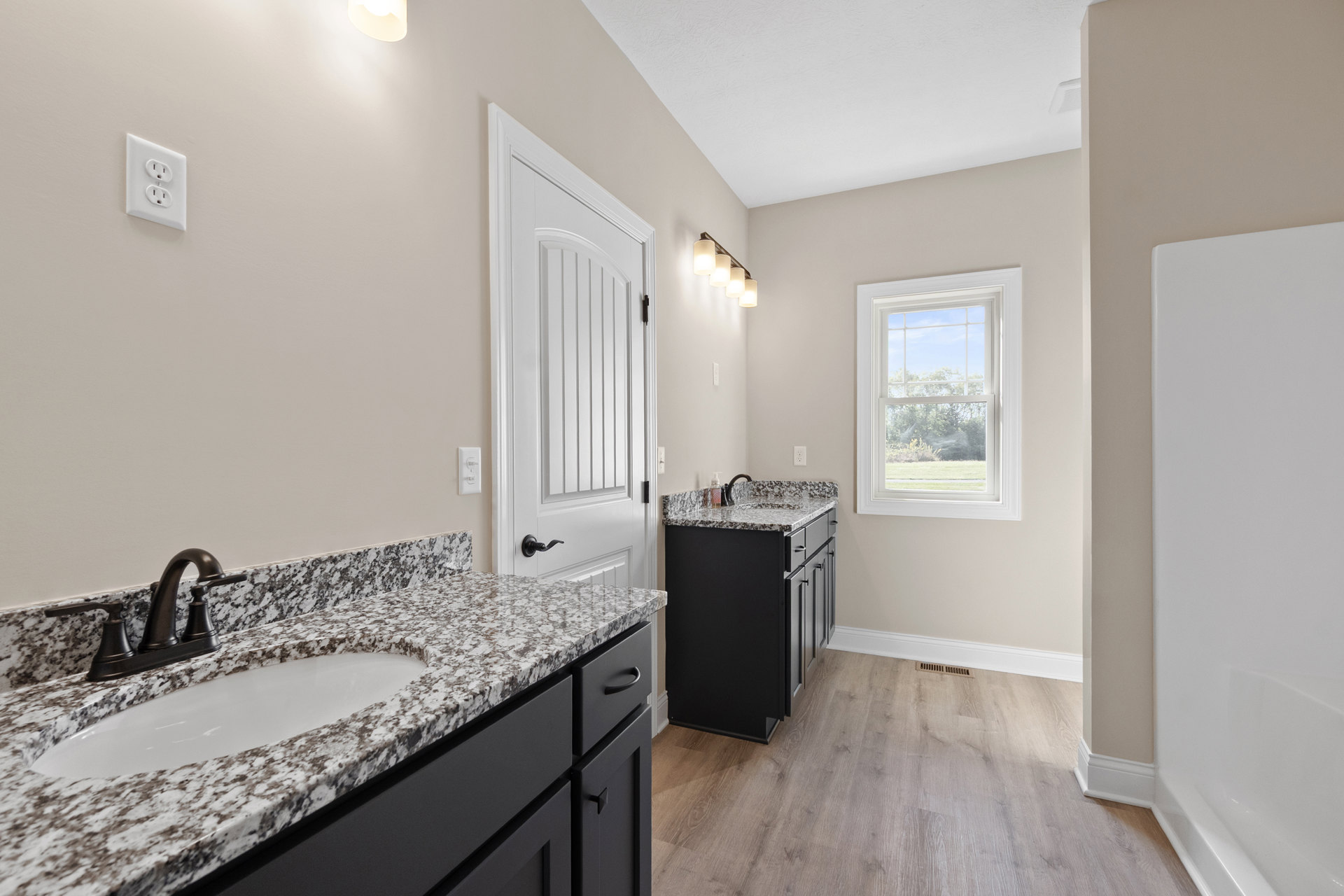 Bathroom featuring marble countertops, wood flooring, white sink with chrome faucet, black kitchen island with marble top, cabinetry, electrical outlet, and window overlooking