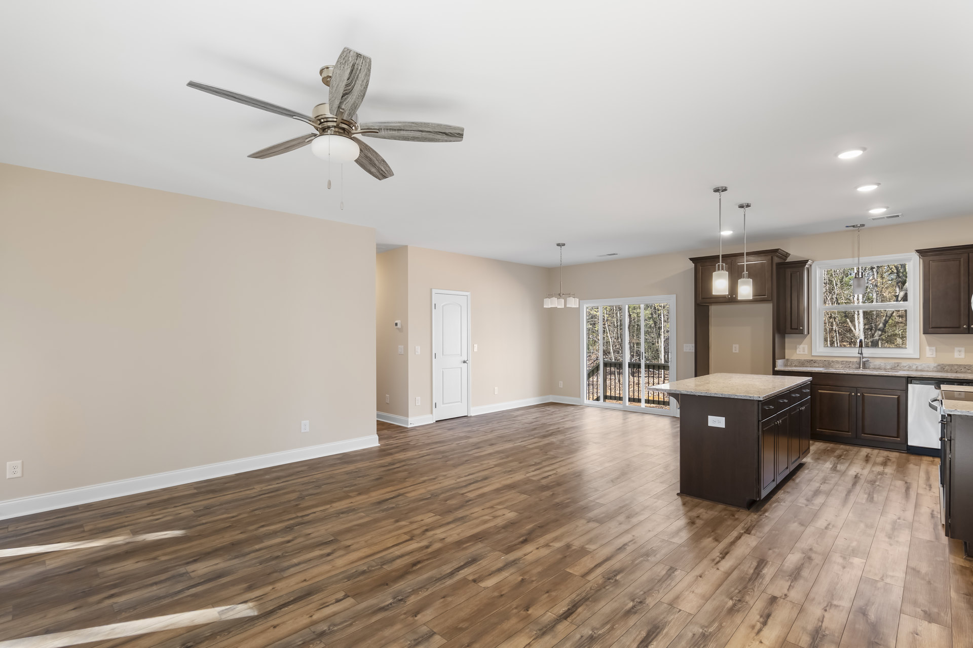Spacious open floor plan featuring a kitchen island with marble countertop, hardwood flooring throughout kitchen and living area, ceiling fan with light fixture, white door with