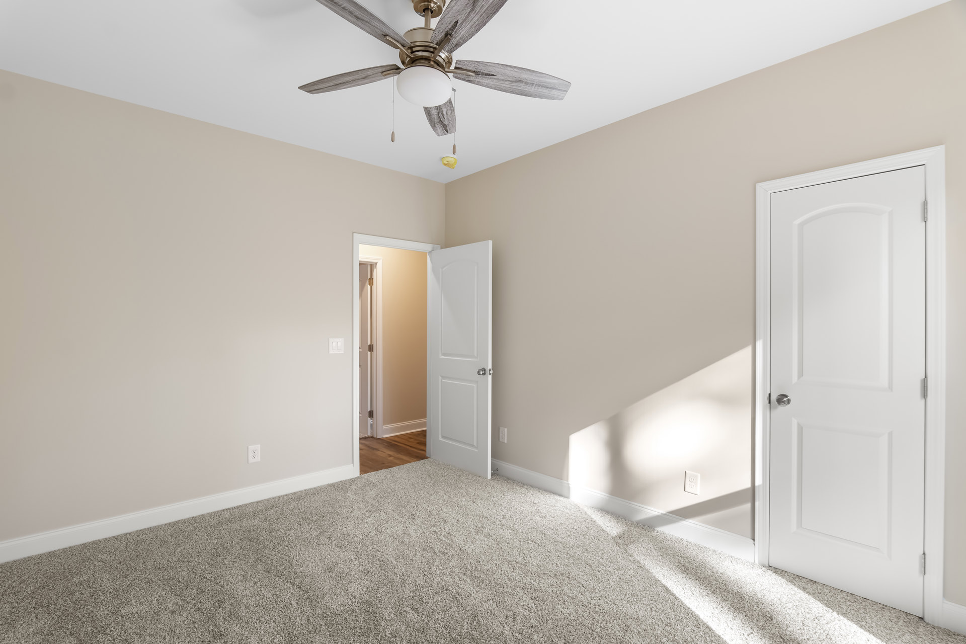 Bedroom with white carpet, ceiling fan with light fixture, two white doors with silver knobs, pale walls, and crown molding.