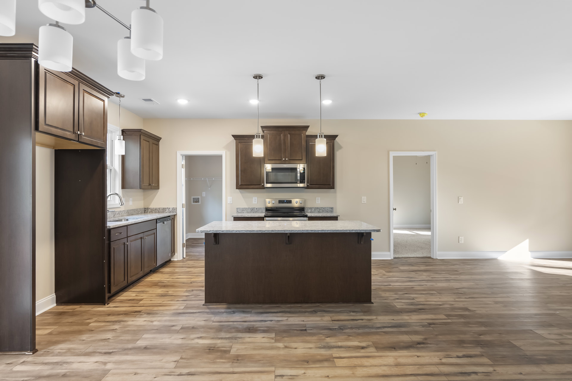 Spacious kitchen featuring a large central island with white cabinetry, stainless steel appliances including oven and microwave, wood plank flooring, stone countertops, and a dark