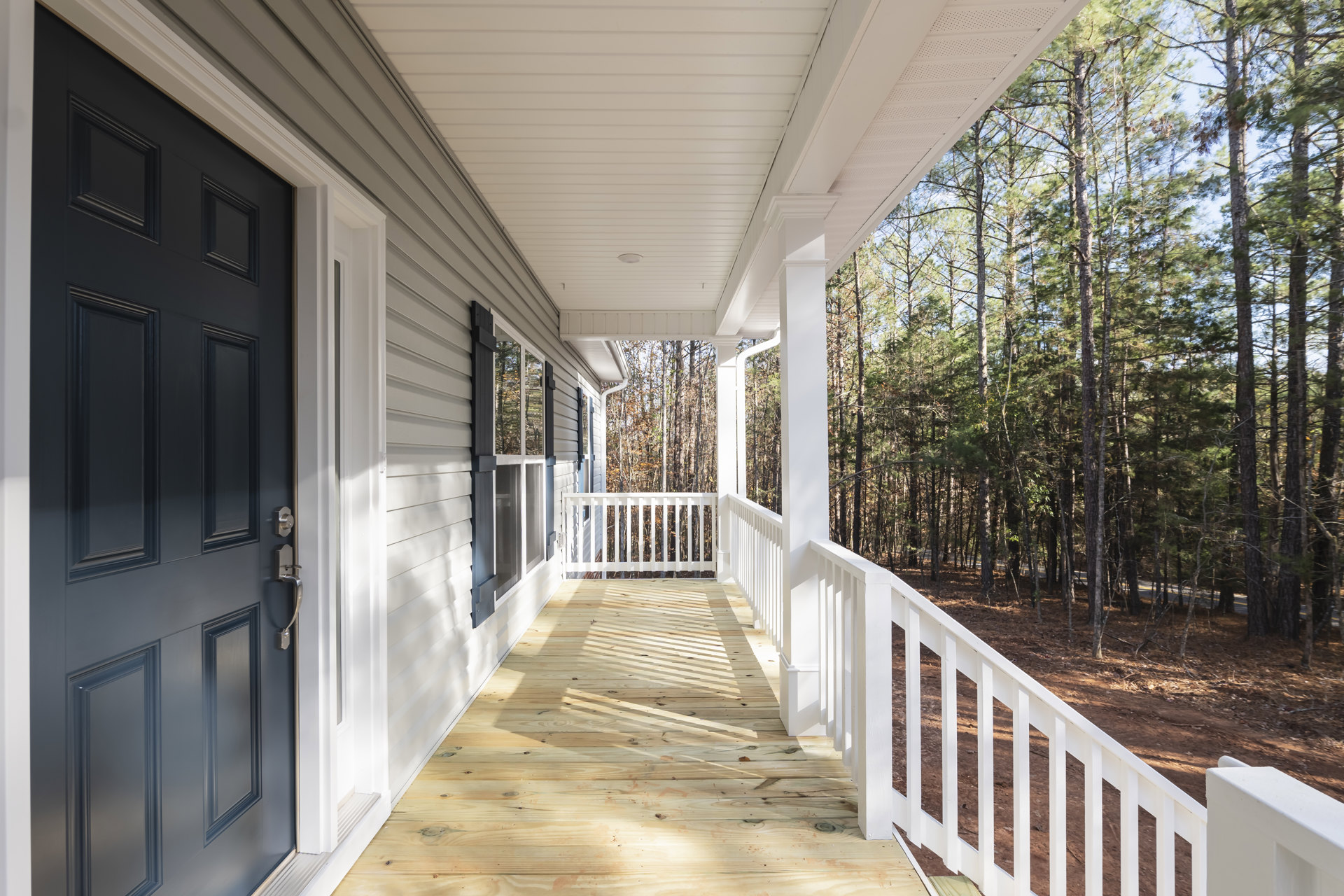 Blue front door framed by white railing on a wood porch, with trees visible in the background
