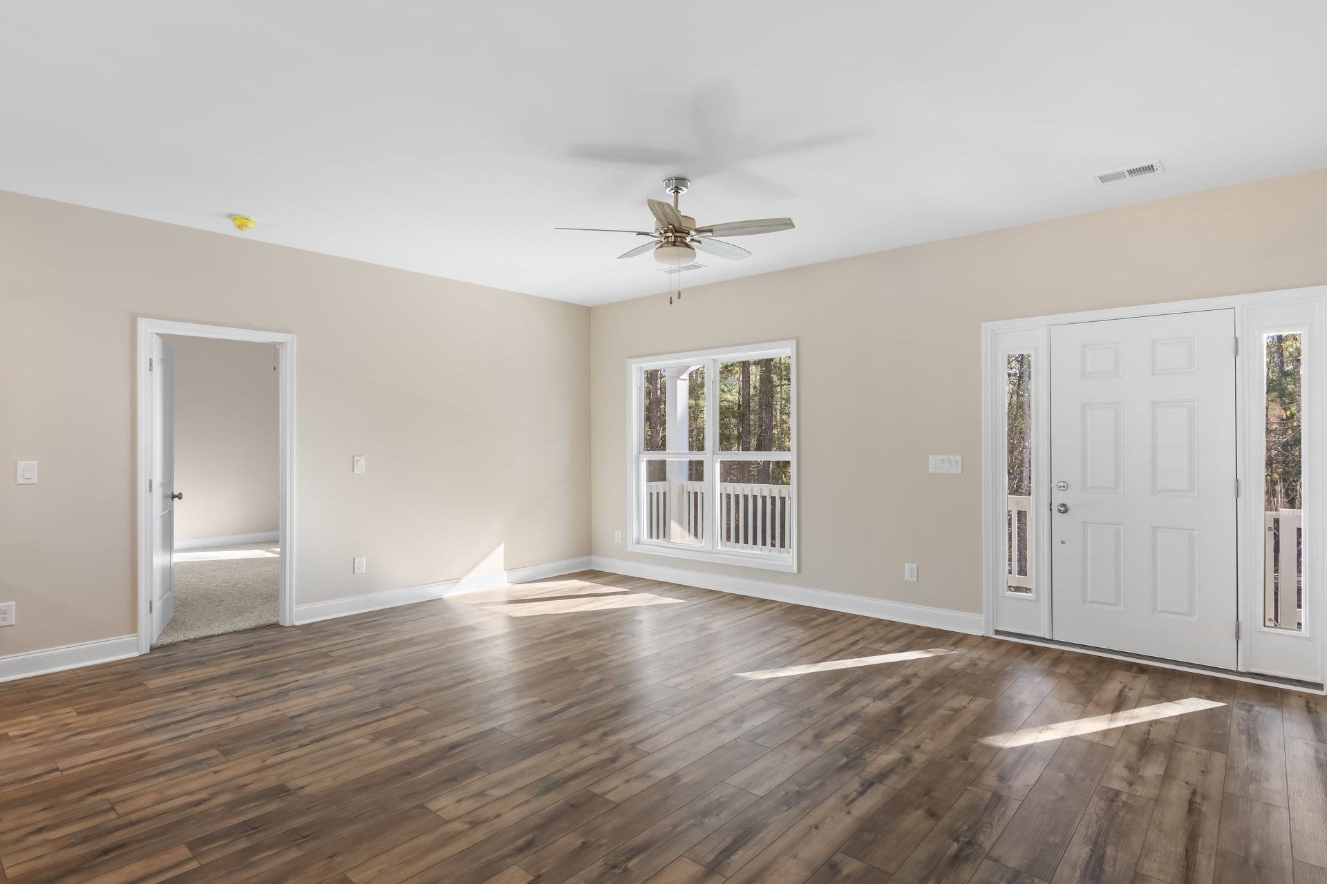 Wood flooring with white walls, ceiling fan with light fixture, large window showing trees outside, white door with glass panels