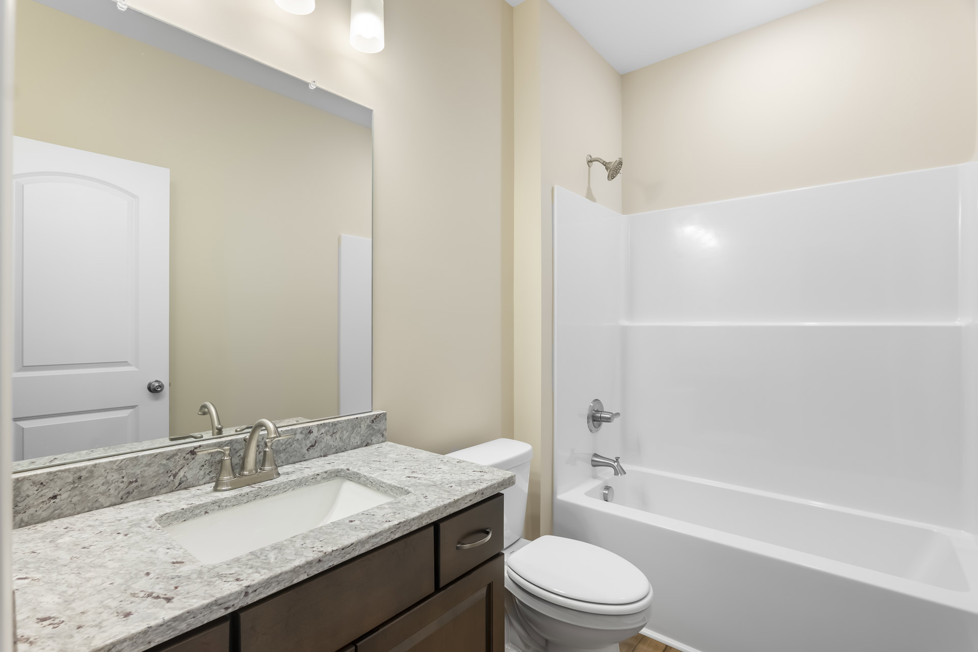 Bathroom with white bathtub, closed toilet, rectangular sink with chrome faucet, wall-mounted mirror, light tile flooring, and white door with square trim