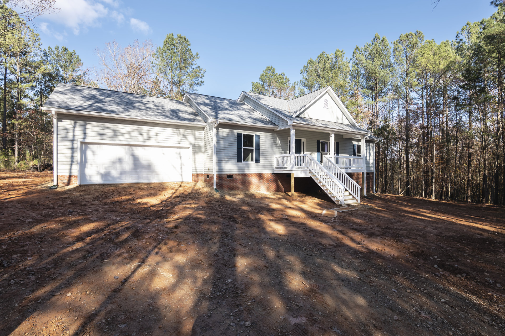 Two-story home with white exterior, attached garage, white staircase leading to front entrance, dirt driveway, and surrounding trees under a cloudy sky