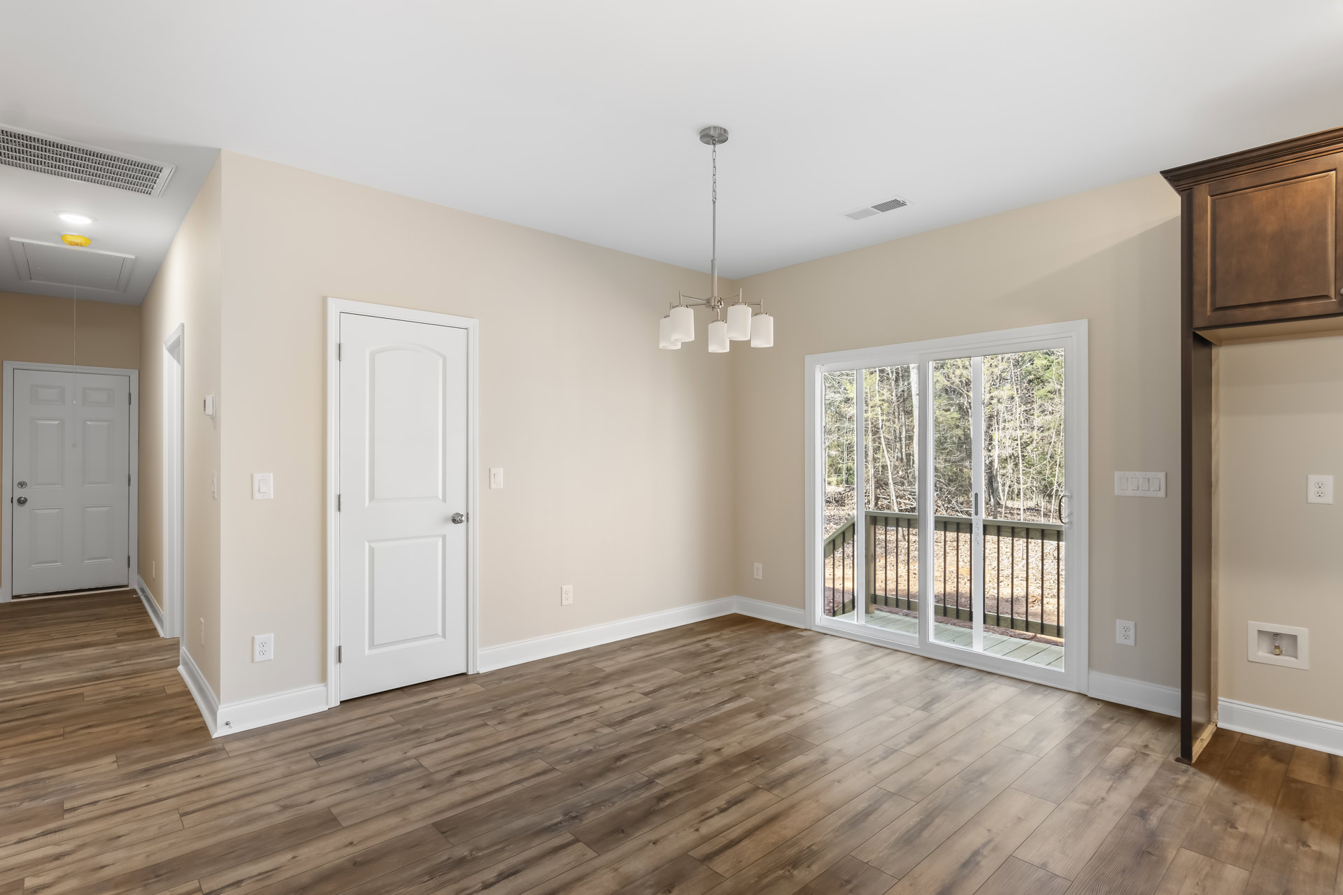 White walls and ceiling, hardwood floor, white door with silver handle, sliding glass door opening to deck with trees, silver ceiling chain.