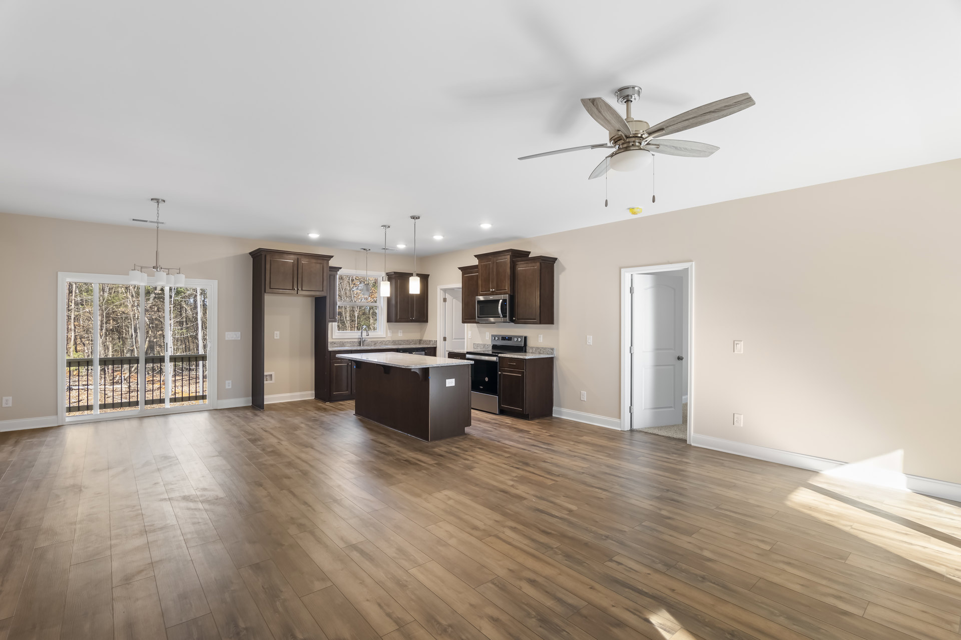 Spacious living room with laminate wood flooring, ceiling fan with light fixture, open kitchen featuring a marble-topped island, stainless steel microwave, white door with silver
