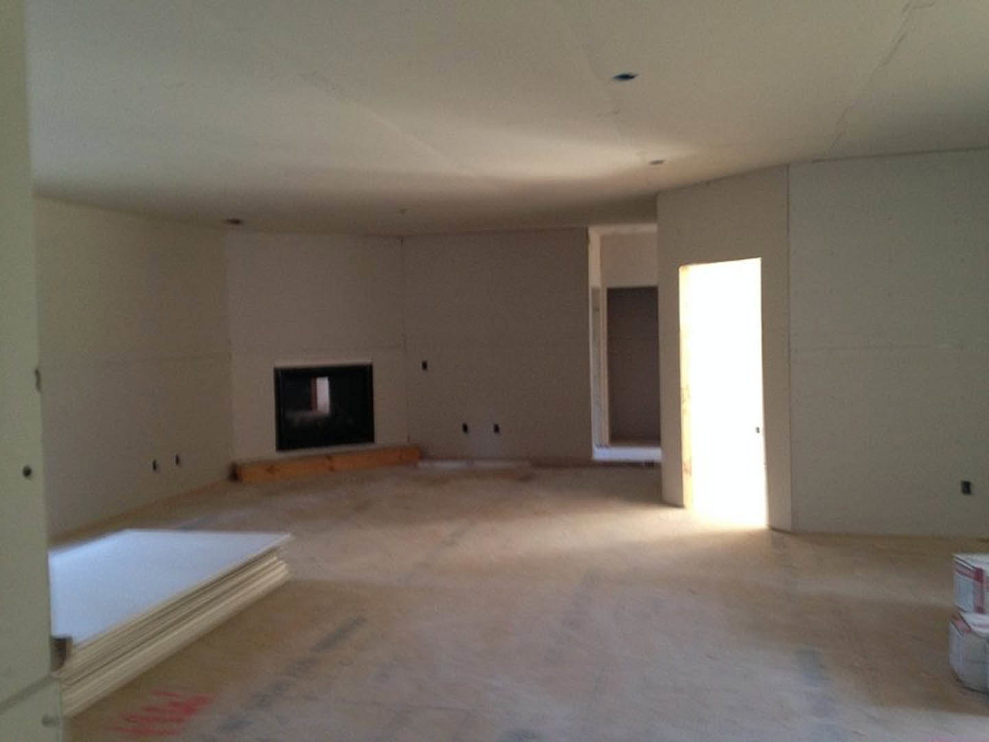Living room with plaster walls, light wood flooring, two fireplaces, and a white door illuminated by sunlight