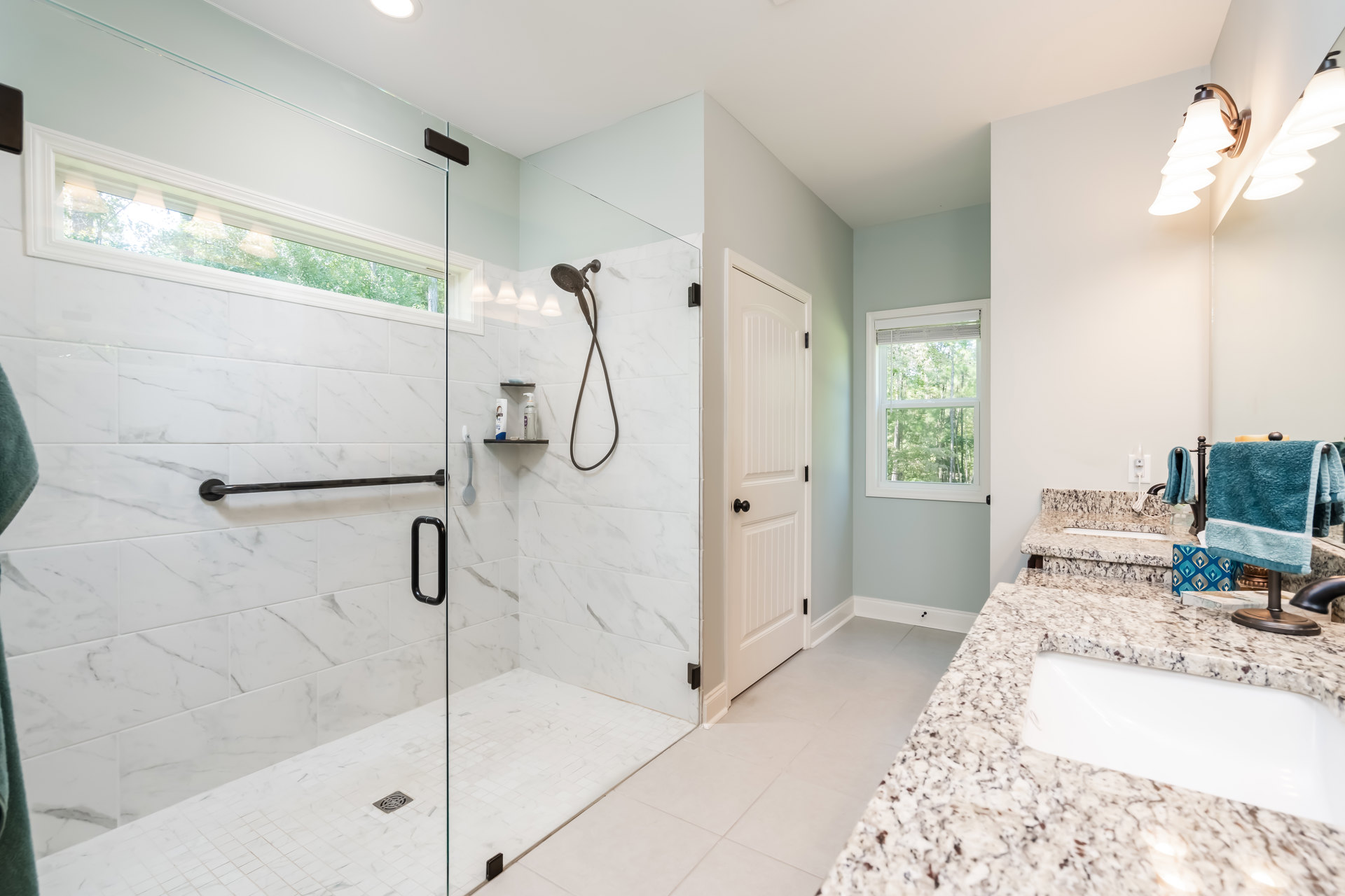 Bathroom featuring marble countertops, glass shower enclosure, towel hanging on wall, window with trees visible outside, and modern plumbing fixtures