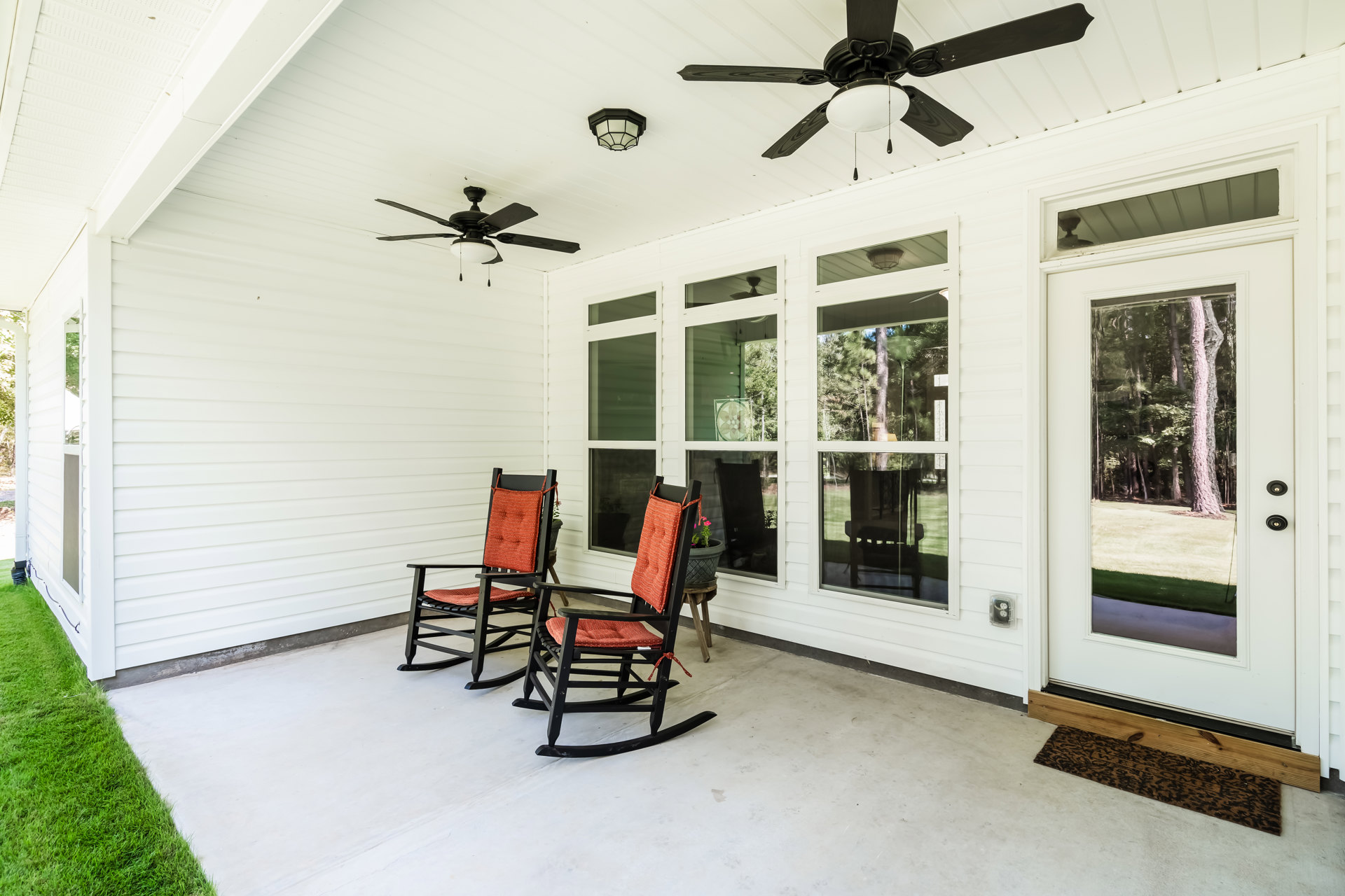 Covered porch with white rocking chairs, ceiling fan with light fixture, stained glass window featuring floral design, and wood door.