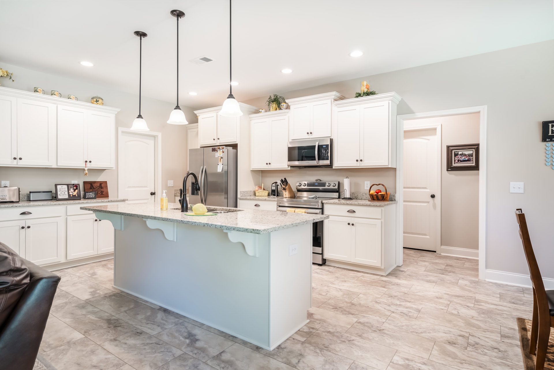 White kitchen with shaker cabinets, stainless appliances, large central island with quartz countertop, wood flooring, and refrigerator decorated with magnets and photos.