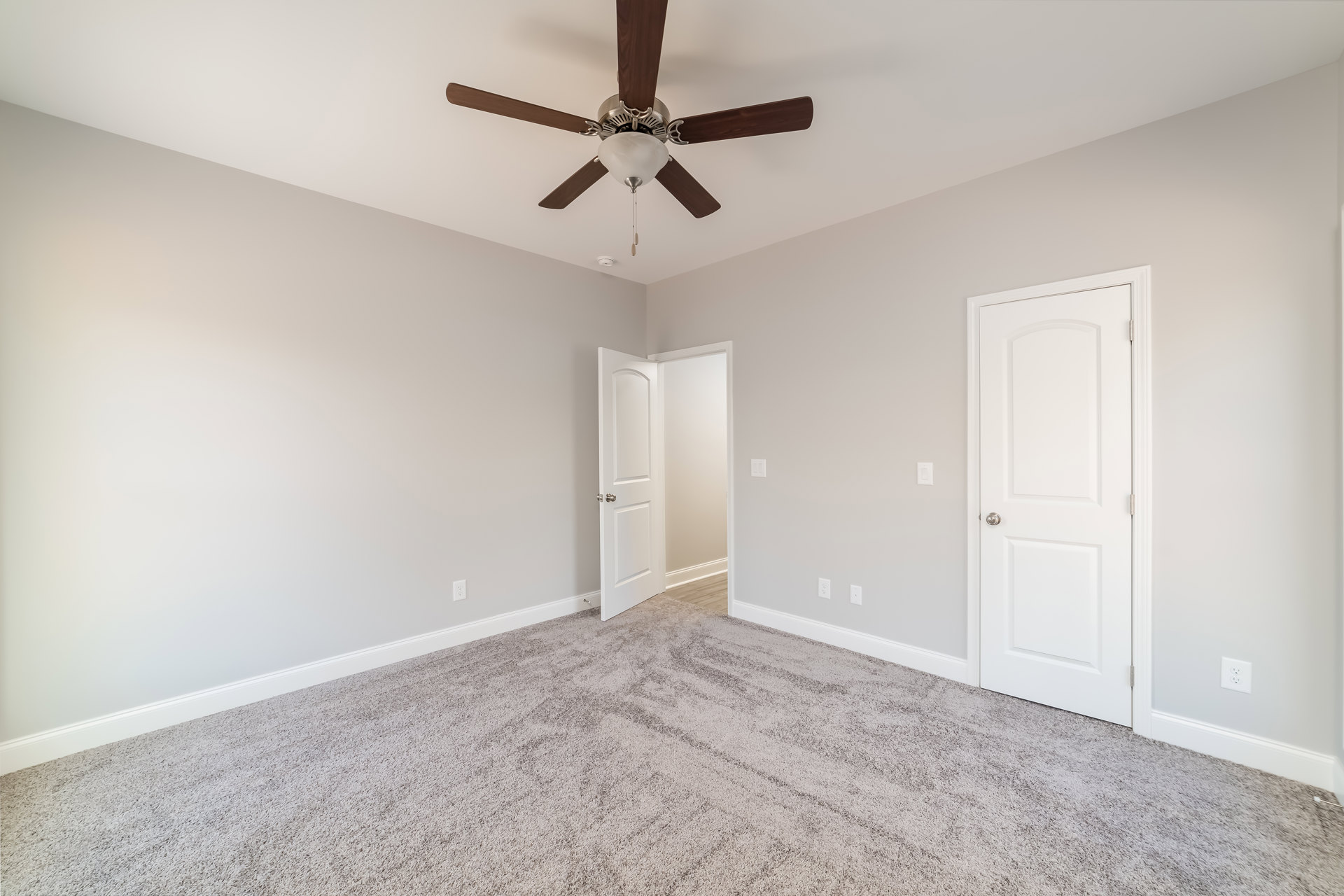 Carpeted room with white walls, ceiling fan featuring light fixture, two white doors with silver knobs, crown molding along ceiling edges