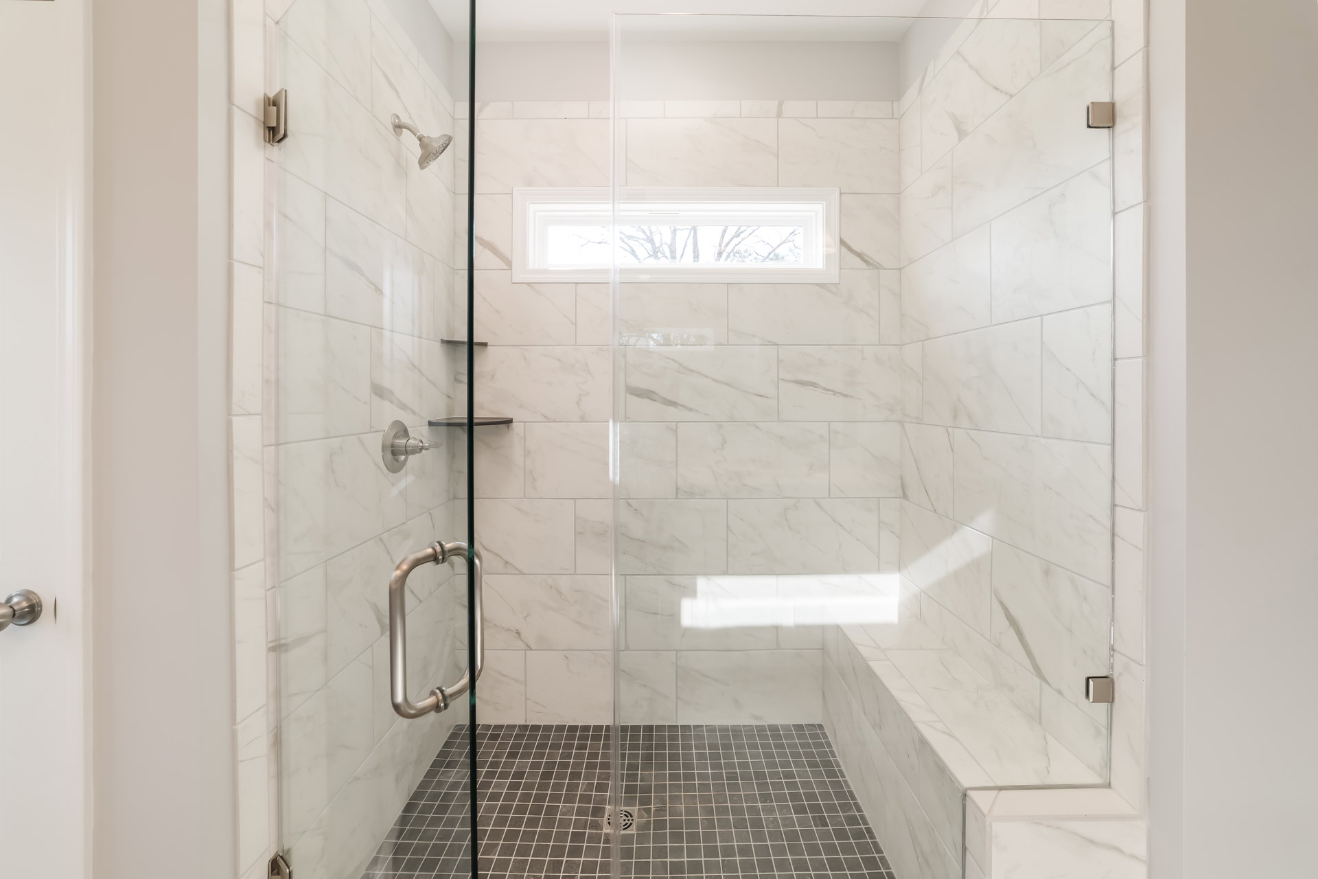 Bathroom with glass shower enclosure, marble tile walls, frosted glass window, chrome shower head, and linear shower drain