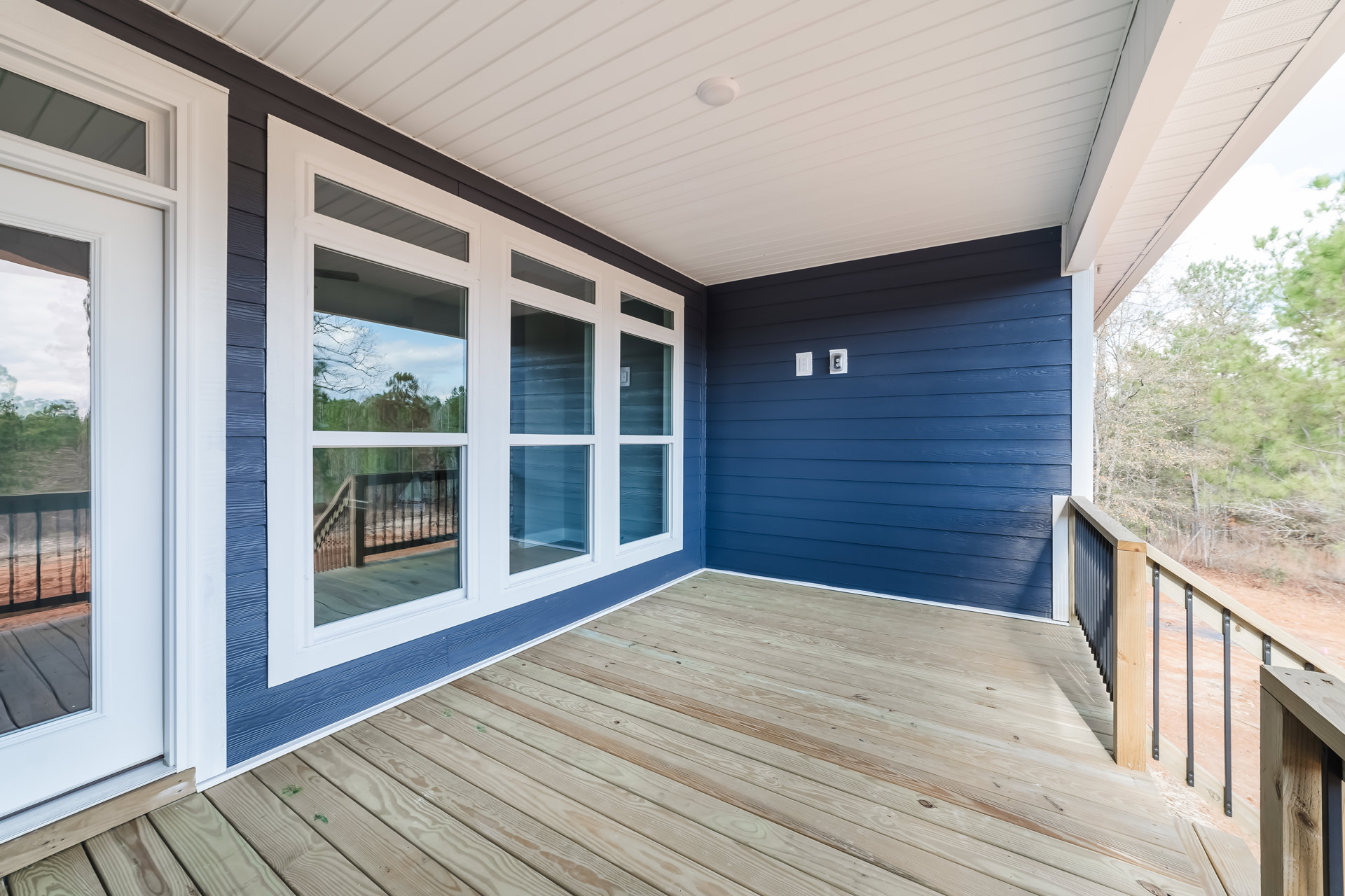 Wooden deck with blue accent wall, large windows, white ceiling with recessed light, and view of trees through window
