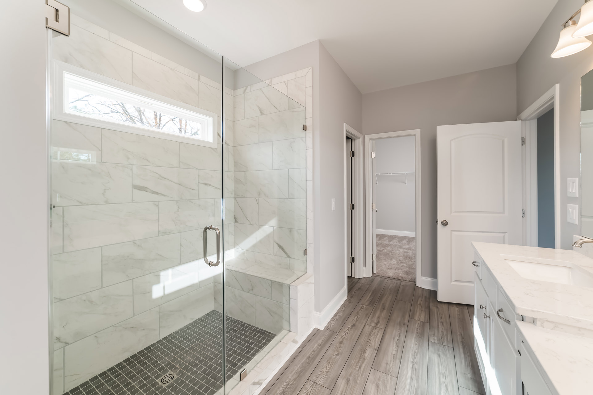 Bathroom with glass shower enclosure, wood flooring, white vanity with silver handles, and modern fixtures