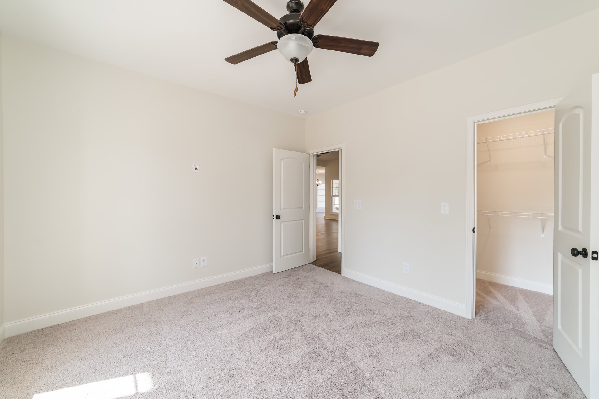 Ceiling fan with light fixture mounted on white plaster ceiling above neutral carpeted floor, white door with black handle visible in corner of room.