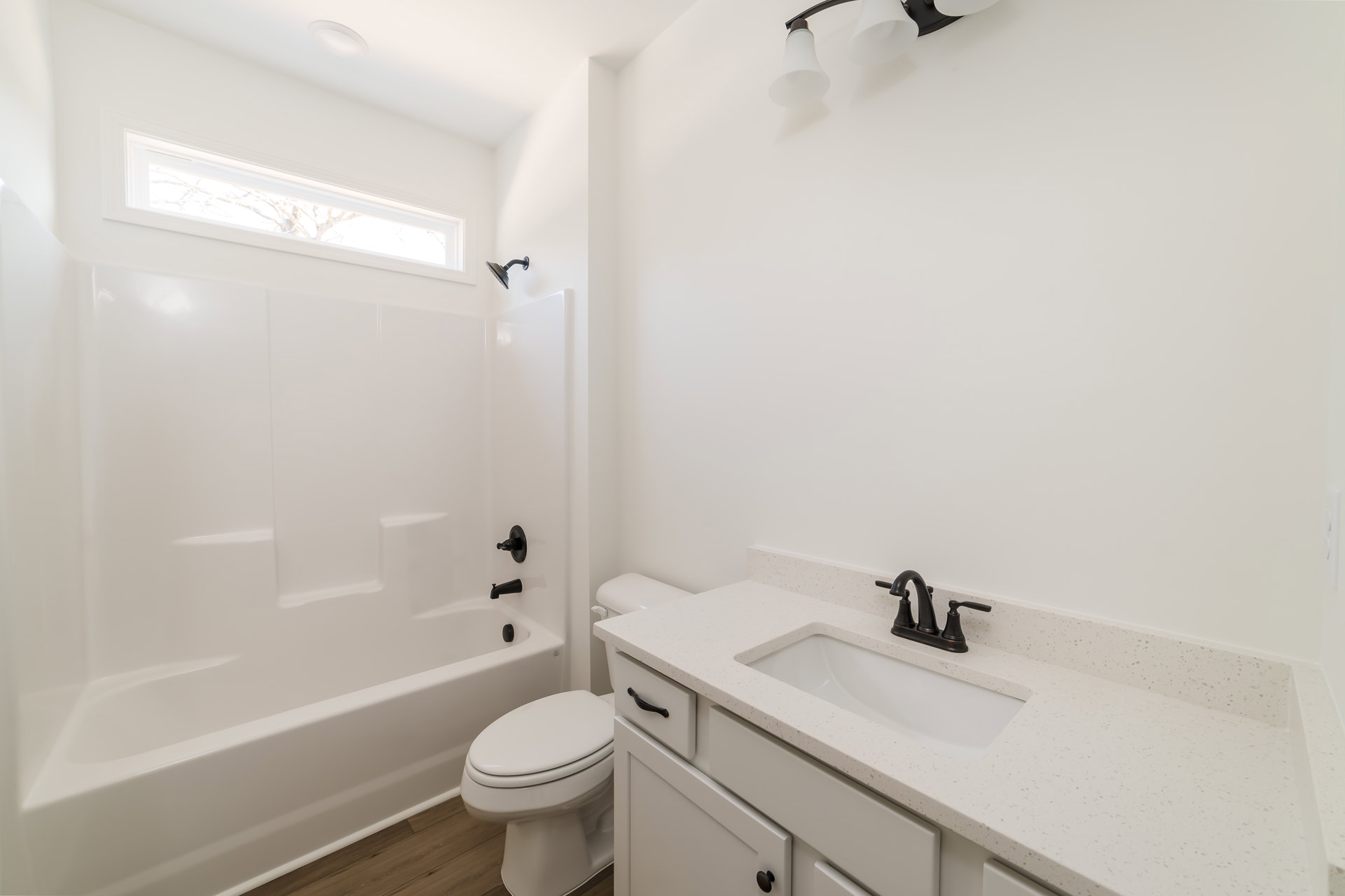Bathroom with white tile walls, modern sink and cabinet, chrome faucet, closed white toilet, wall mirror, and window showing leafy tree outside