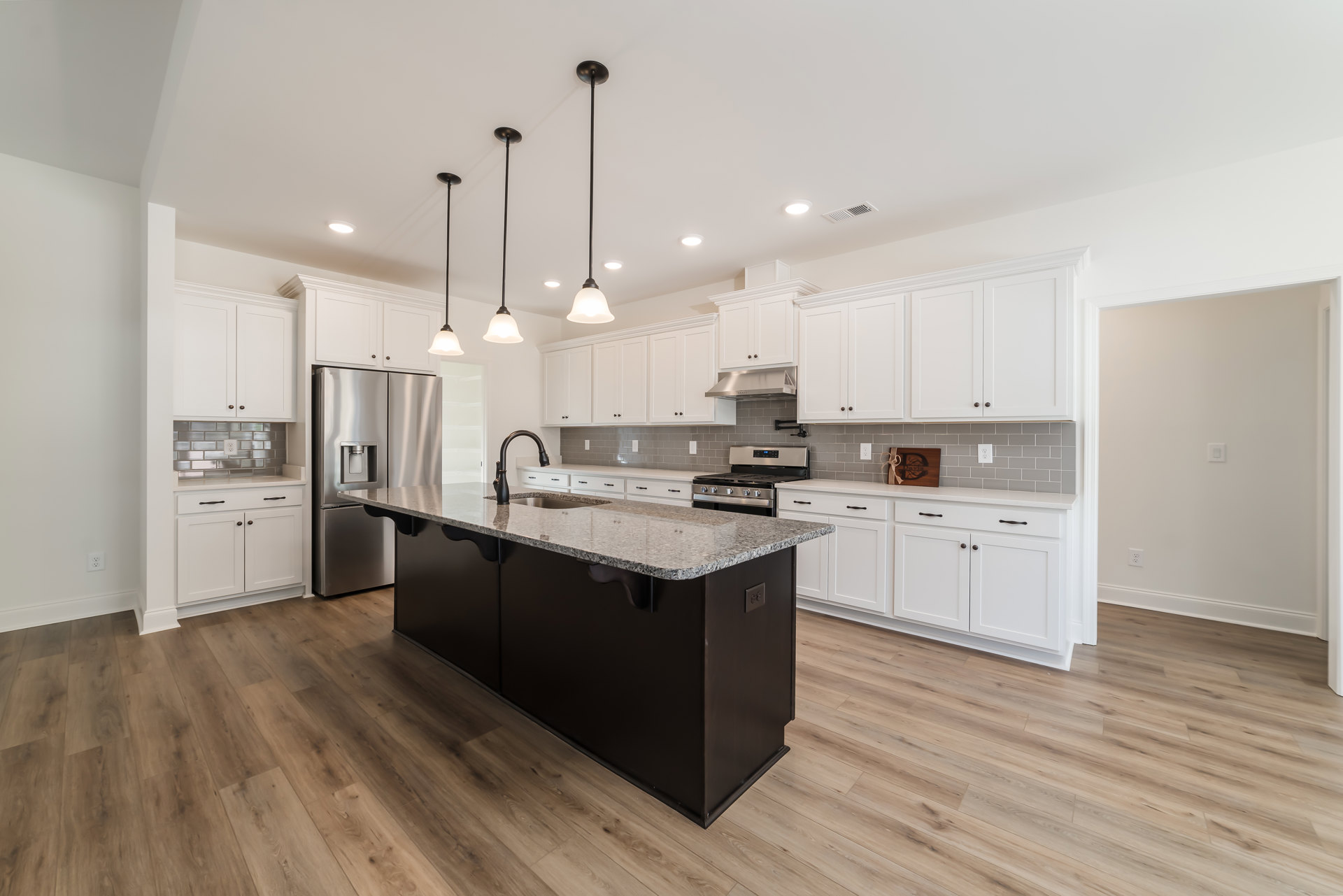 White shaker cabinets, black kitchen island with built-in stove and oven, stainless steel refrigerator with water dispenser, light countertops, hardwood flooring, recessed