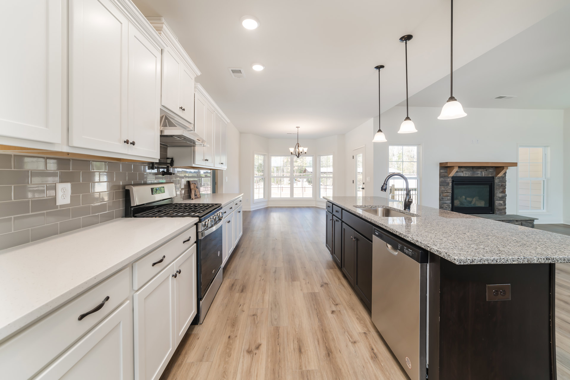 White kitchen cabinets with black handles, stainless steel stove, light stone countertops, undermount sink, and wood flooring