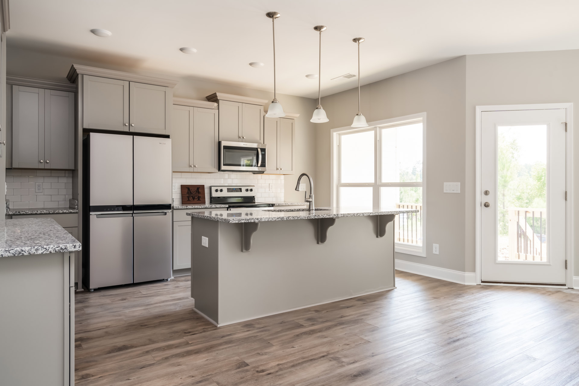 Kitchen with wood flooring, central island featuring white and black countertop, stainless refrigerator with black handle, built-in microwave, white cabinetry, glass-paneled door