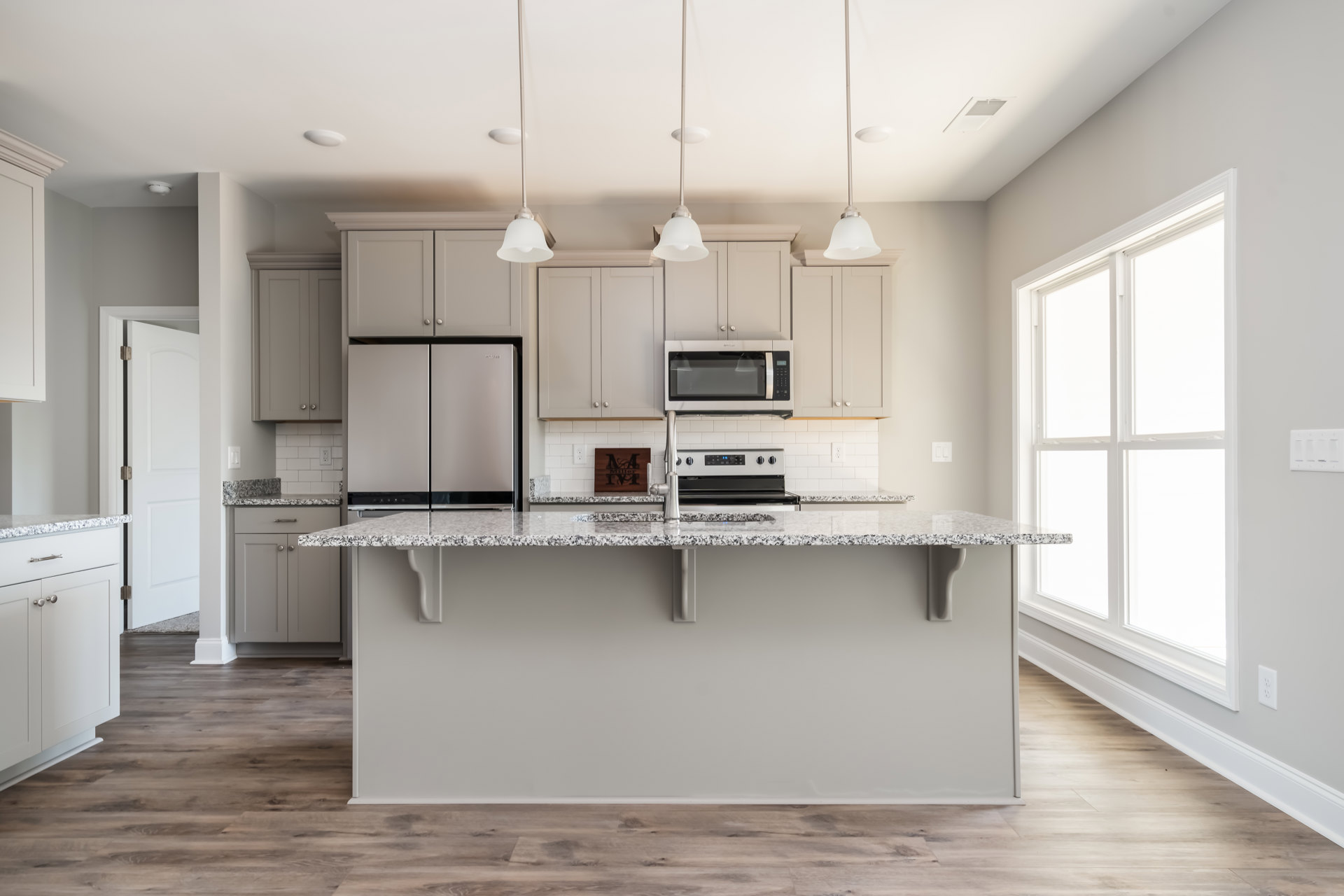 Marble countertop kitchen with white cabinetry, stainless steel refrigerator with black trim, white microwave, wood wall sign, and light-colored flooring