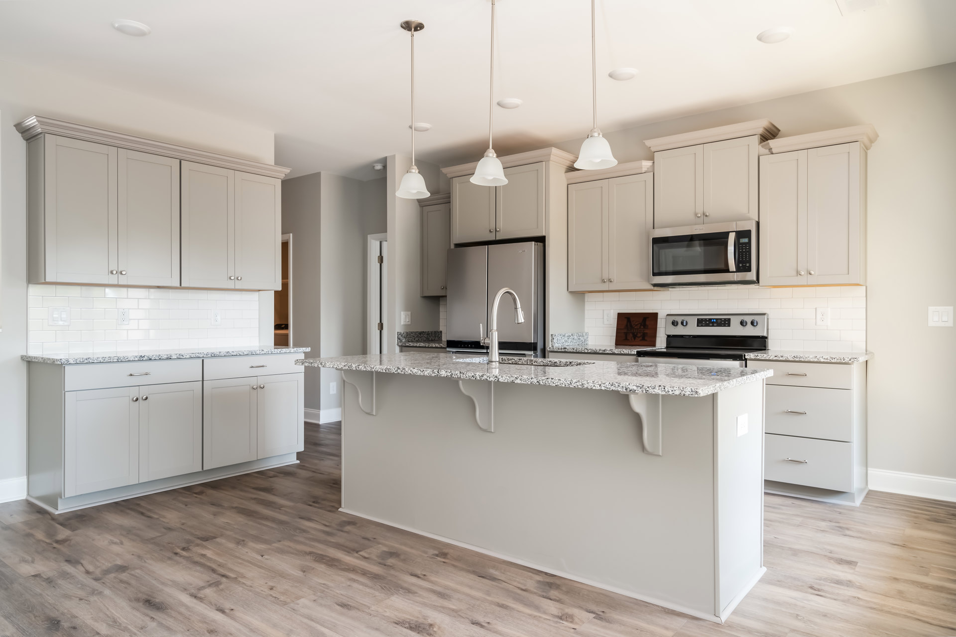 Marble kitchen countertop with stainless steel faucet, white cabinetry, wood flooring, and built-in microwave