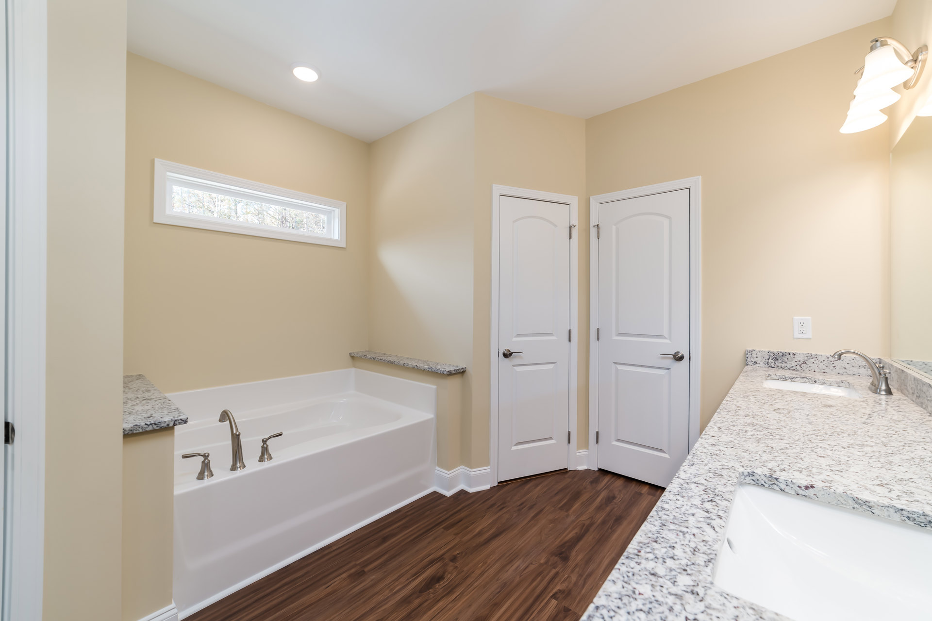 Bathroom featuring a freestanding bathtub with chrome faucets, dual sinks set in a white and black marble countertop, white cabinetry, silver hardware, and a three-light fixture