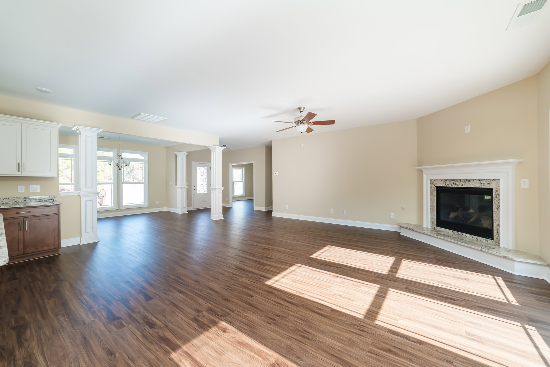 Spacious living room featuring wood flooring, white walls, glass-screen fireplace, marble countertop, ceiling fan with light fixture, and window with white frame