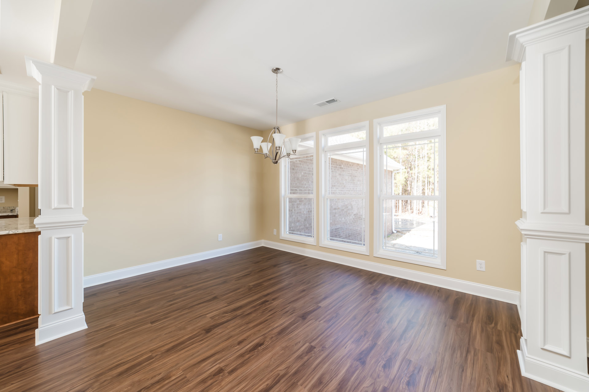 Hardwood flooring in a spacious room with large windows, white walls, decorative molding, and a chandelier; trees visible outside
