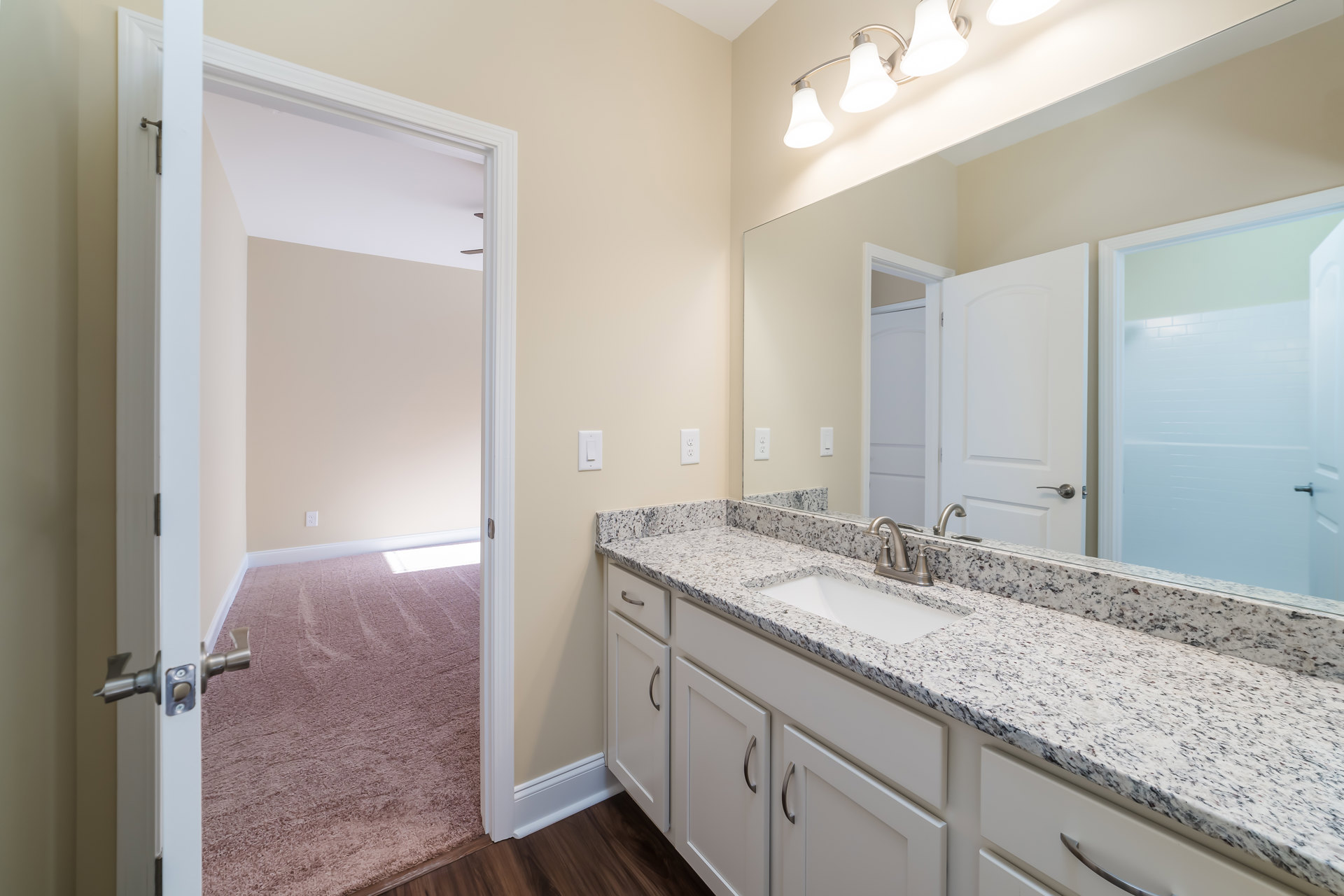 Bathroom with marble countertop, undermount sink, silver faucet, large framed mirror, white door with silver handle, three-light fixture above mirror, light-colored tile