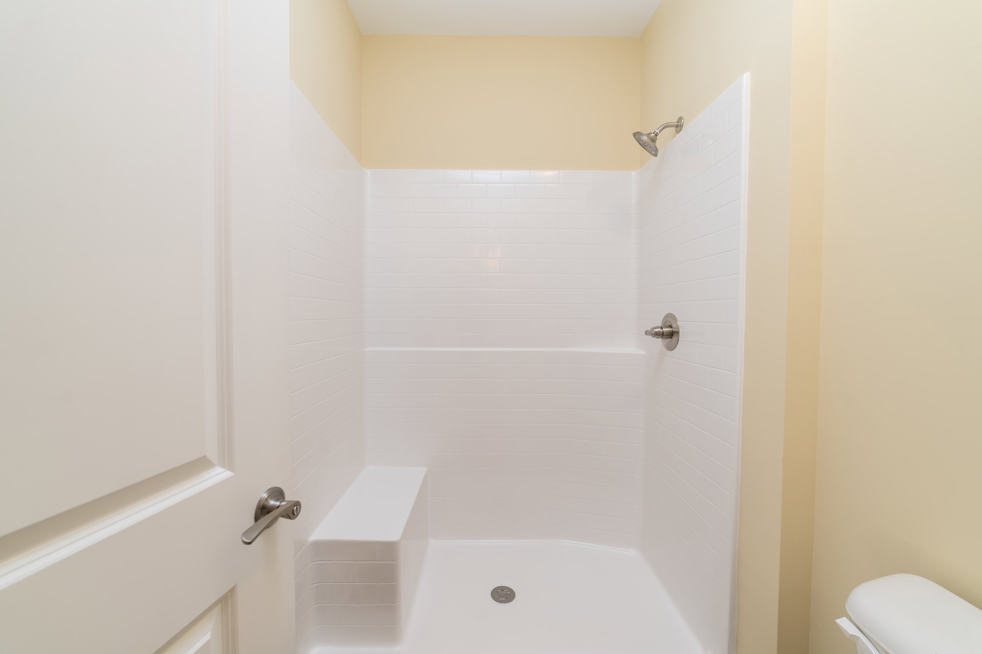 Walk-in shower with white tile walls, built-in bench, glass door, and chrome shower head