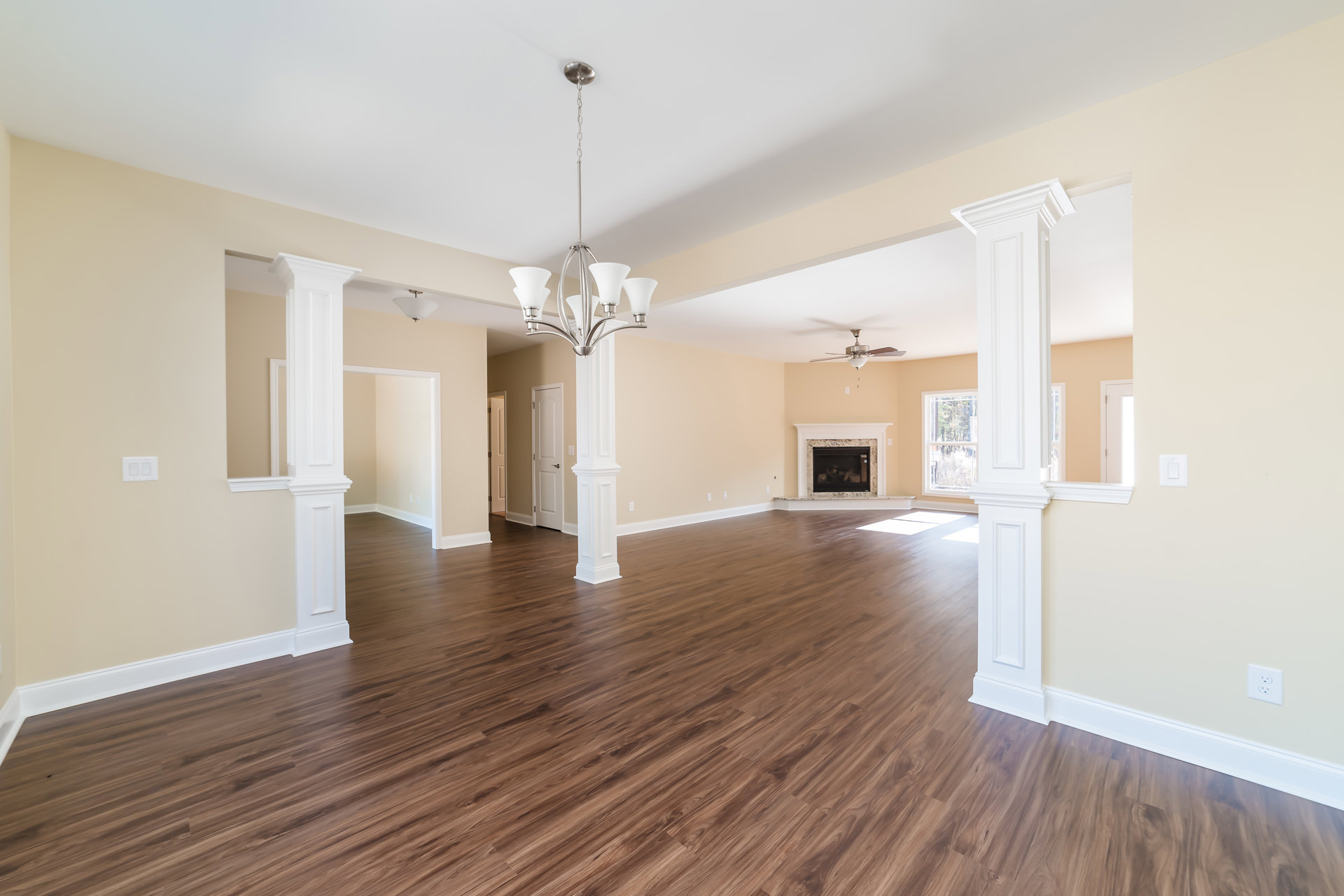 Spacious living area with white columns, hardwood flooring, stone fireplace, and large windows