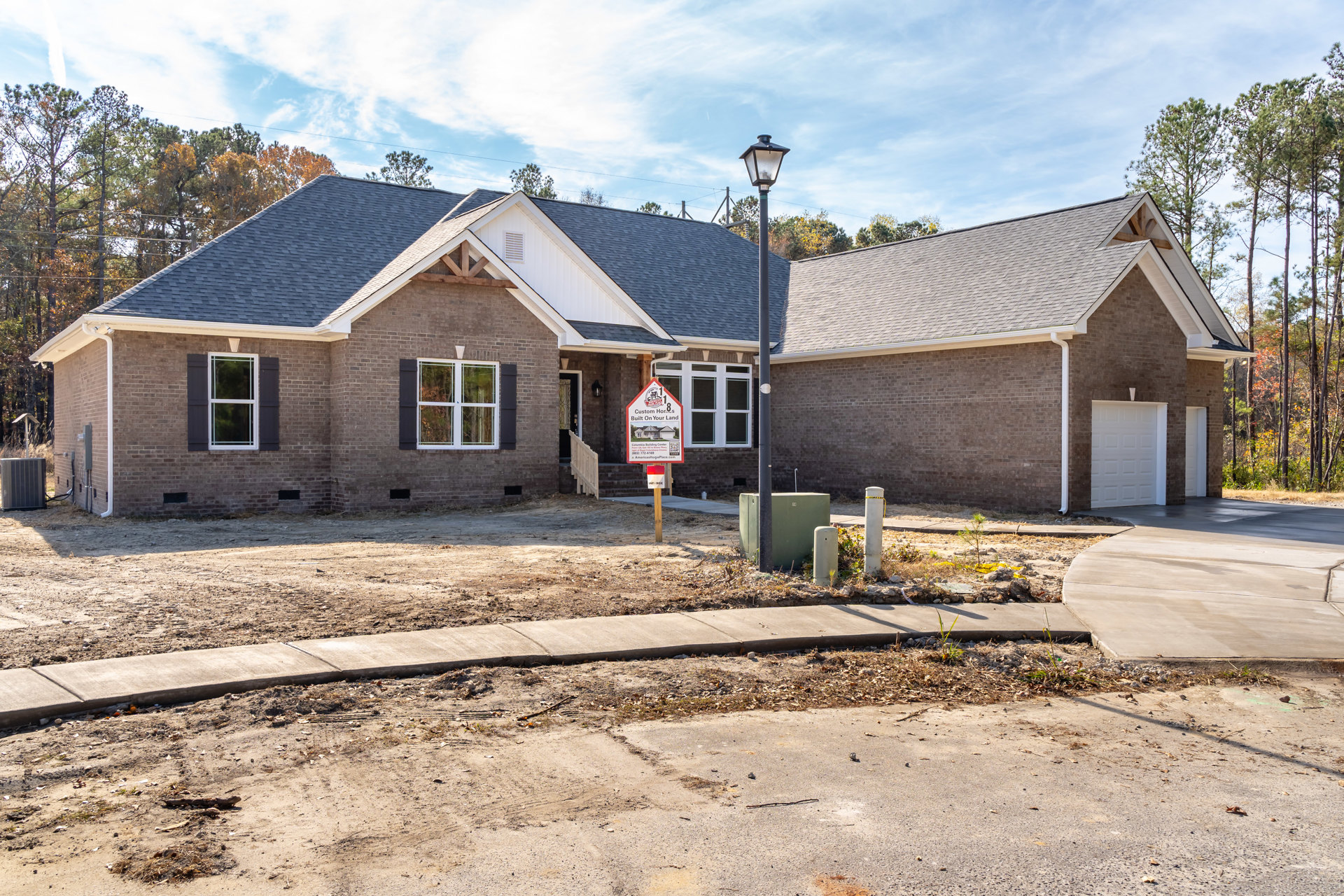 Two-story home with white-framed windows, grey metal utility box near sidewalk, real estate sign on post in front yard, tree and clouds in background