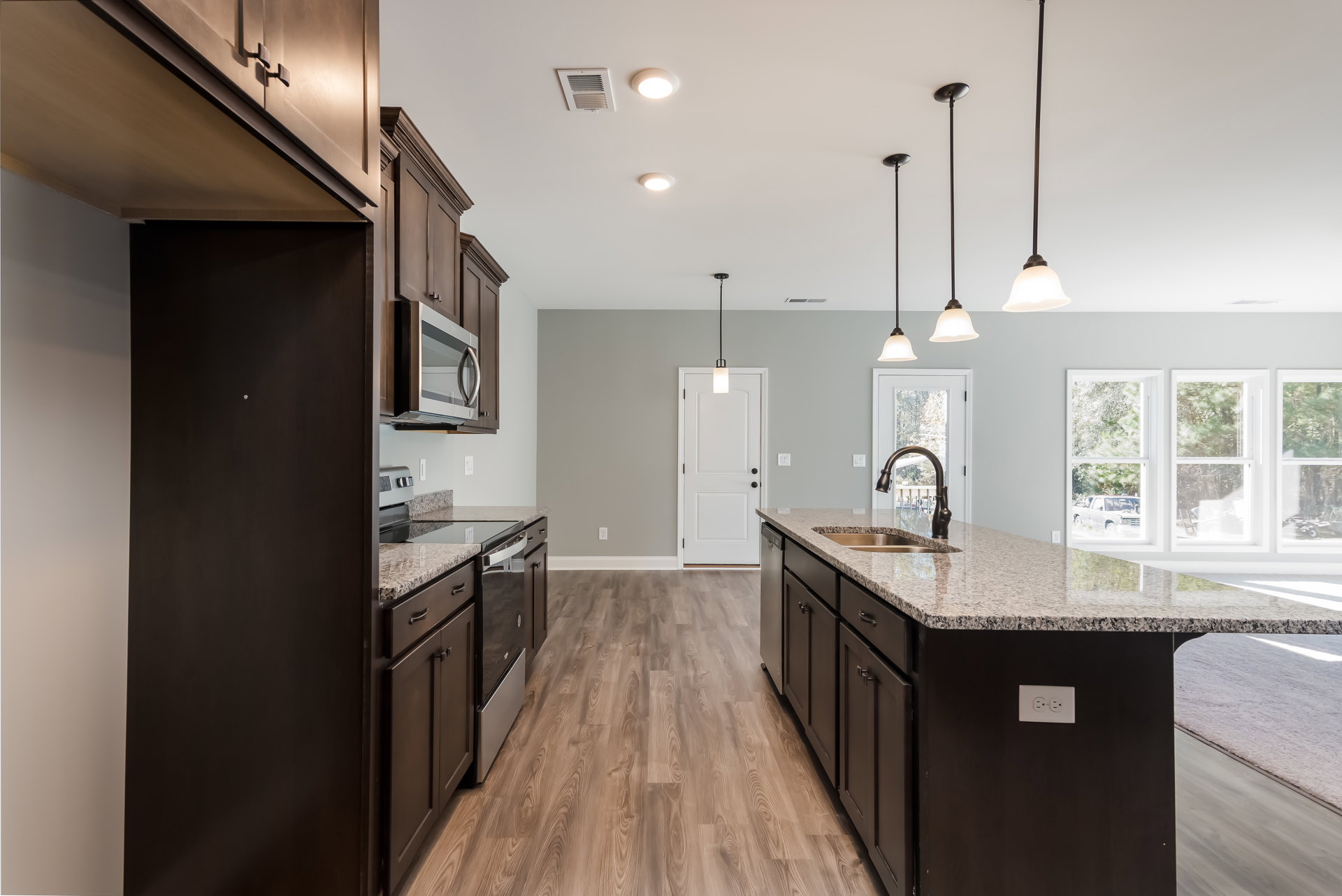 Granite countertops, wood flooring, white cabinetry with black hardware, built-in microwave, stainless steel sink, window overlooking driveway with parked car