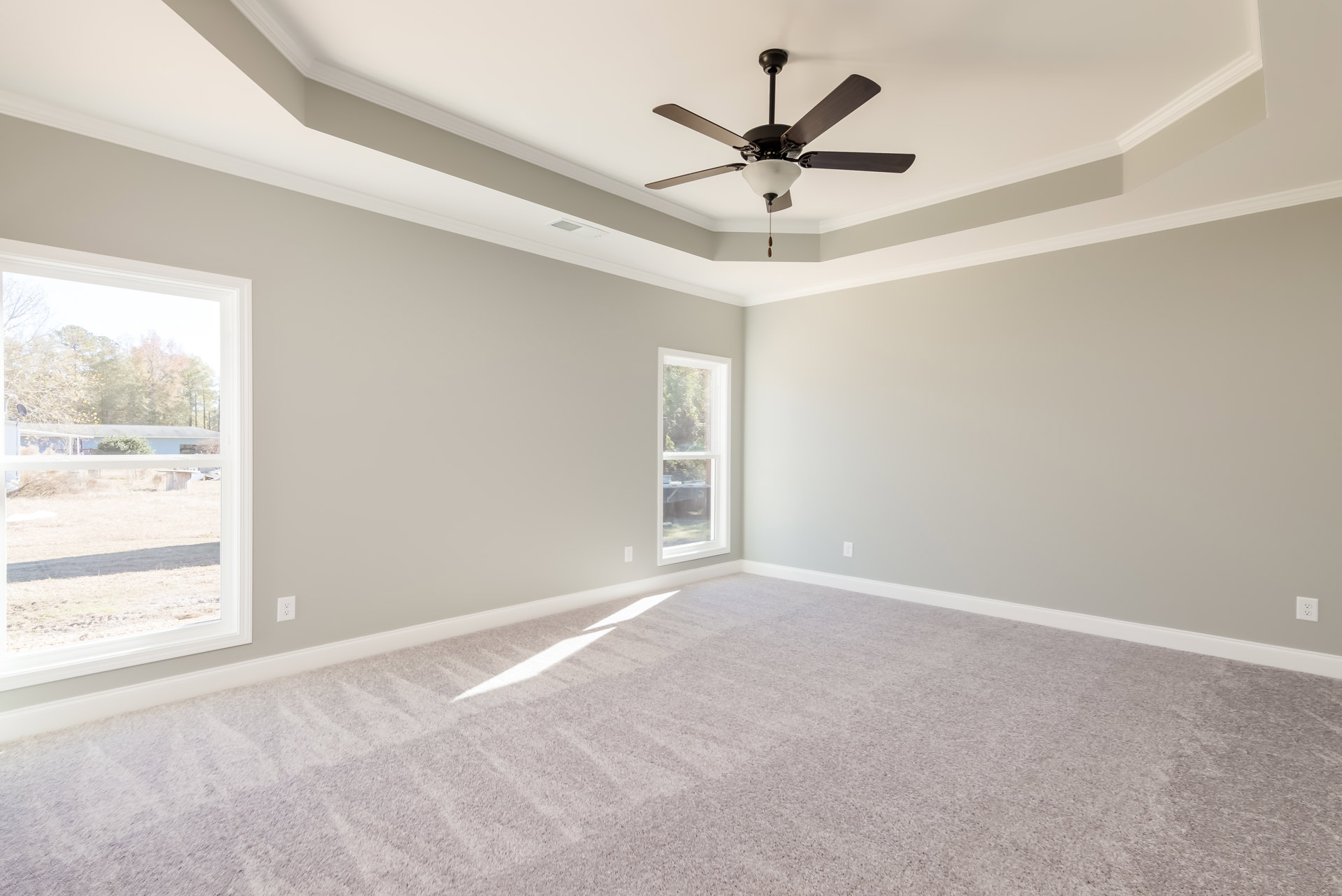 Carpeted room featuring a ceiling fan with light fixture, large window overlooking yard and trees, white walls with crown molding